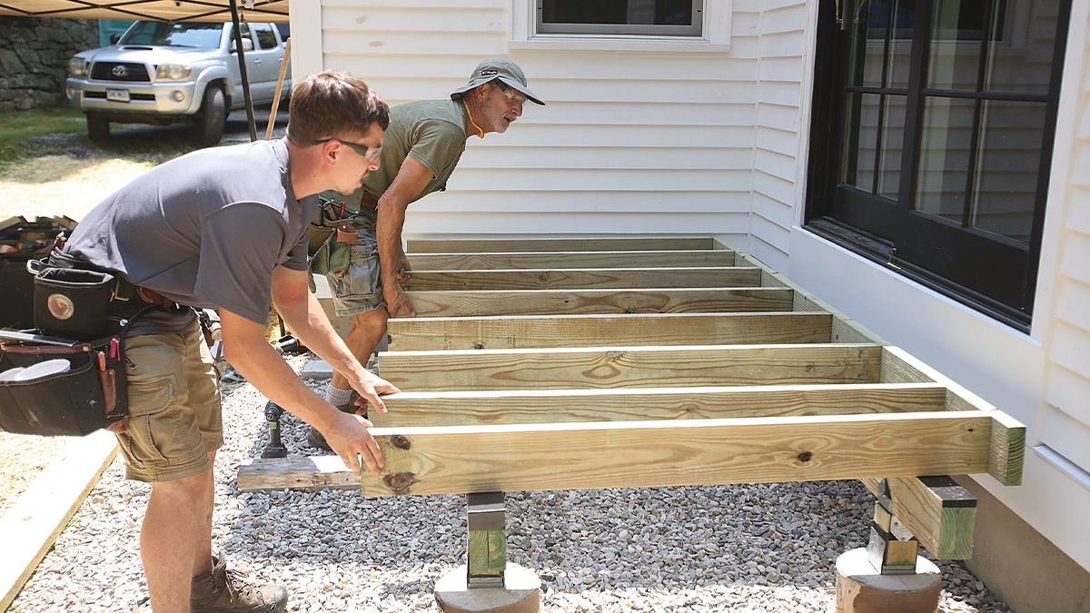 Contractors building a pressure-treated wood deck frame during residential construction.