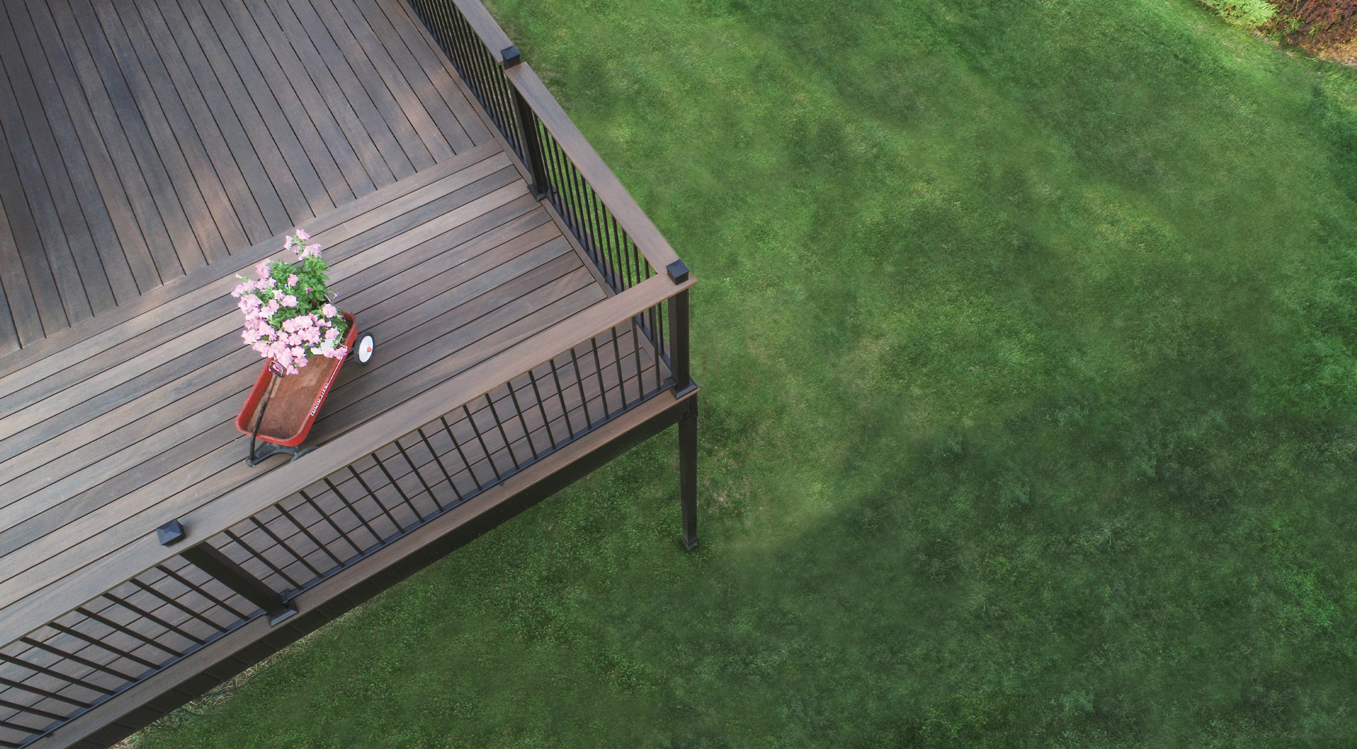 Top view of a wooden deck with black metal railing, featuring a red wagon and a potted flower.