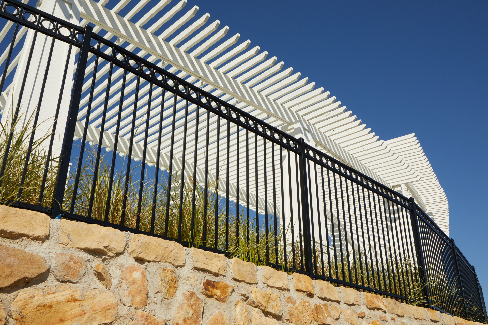 Steel fence with ornamental design on a stone wall, under a white pergola.