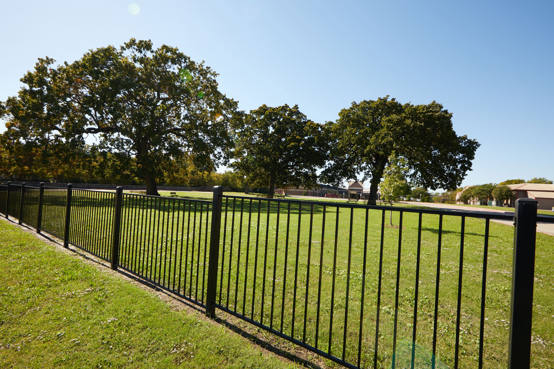 Black metal fencing in the foreground encloses a school in the background.