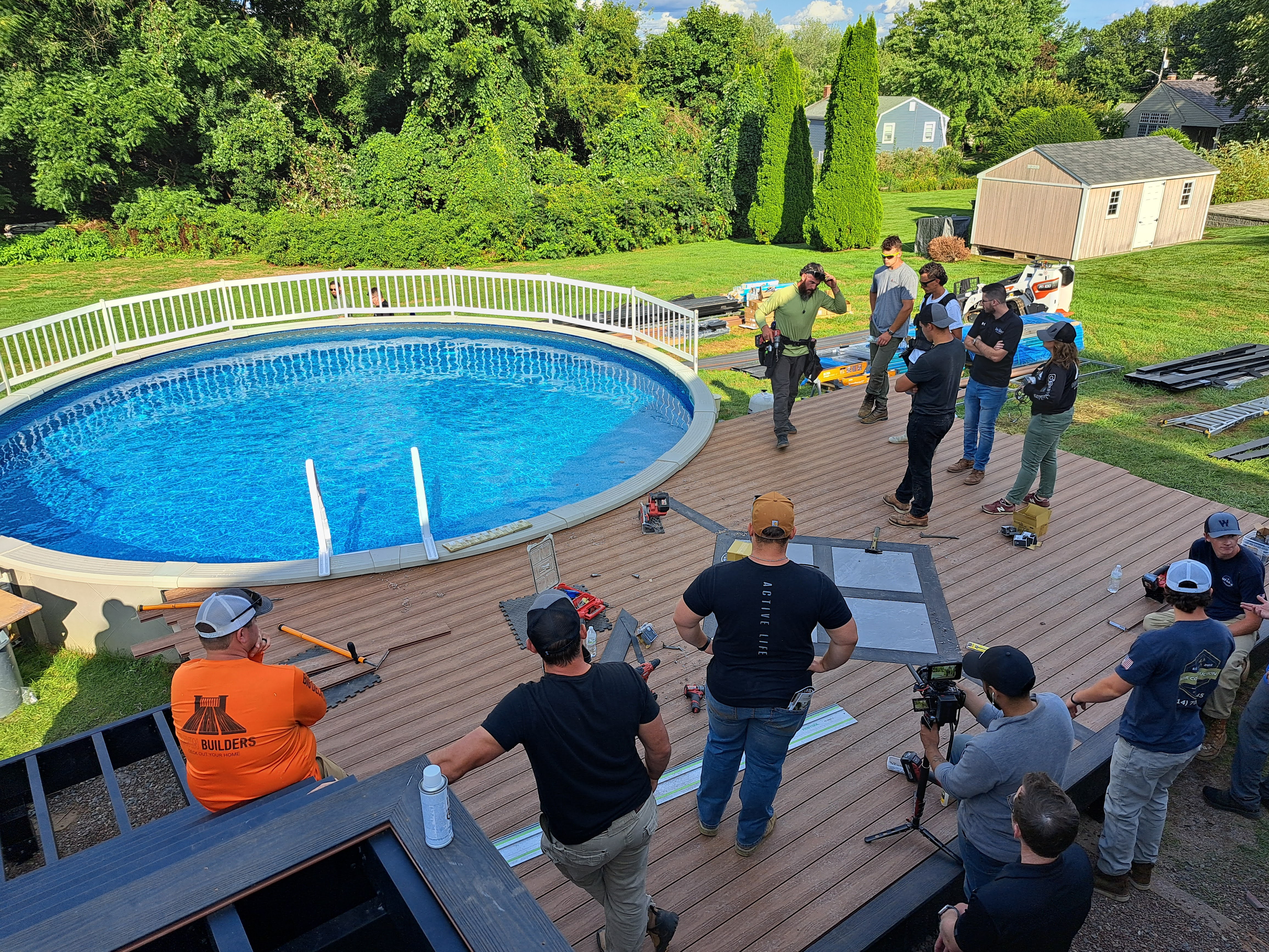 Ravin Builders around a deck framing installation by a pool, led by a builder in a green shirt. 