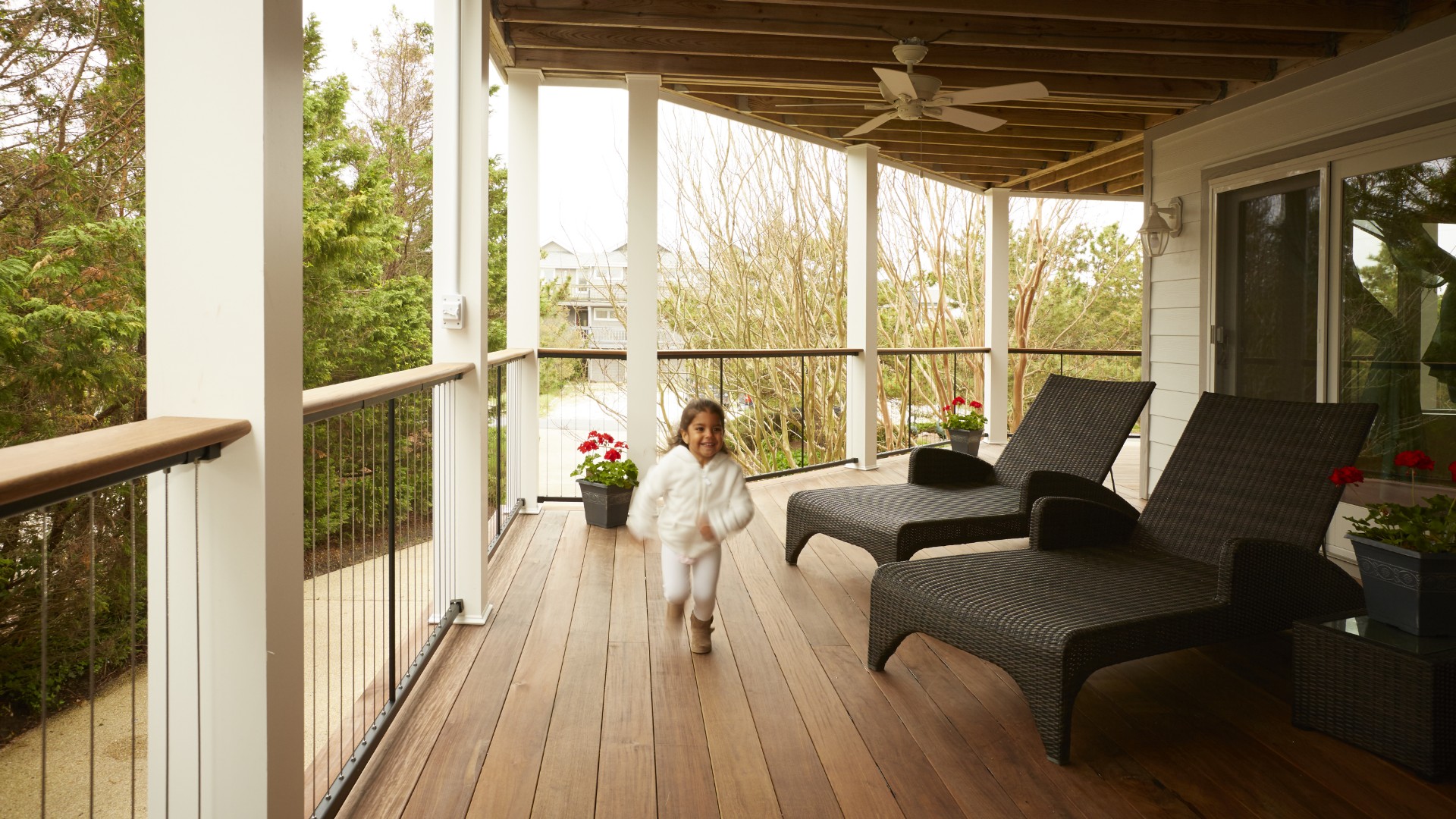 Child running on a wooden balcony with stylish railings and outdoor furniture.