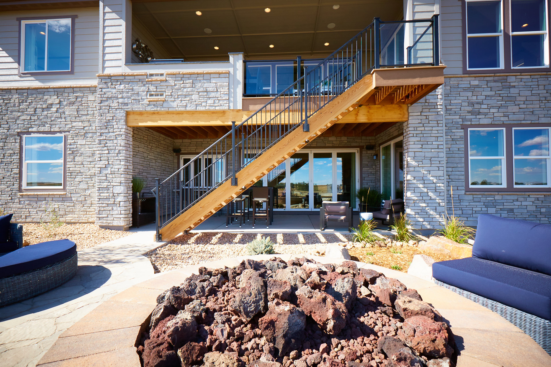 Staircase leading to an upper deck with metal deck railings against a stone home.