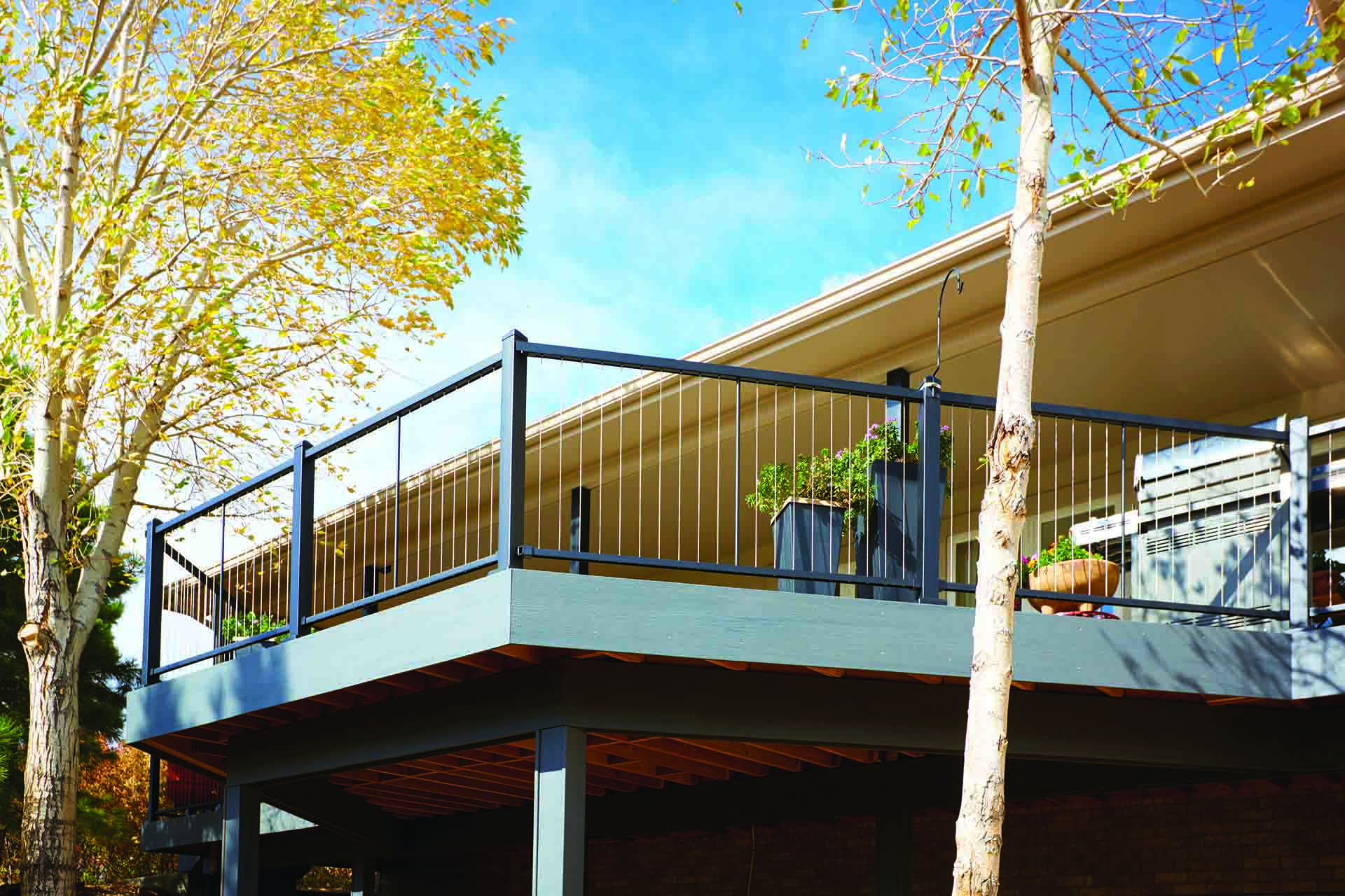 A balcony with cable railing, with potted plants, overlooking a fall landscape.