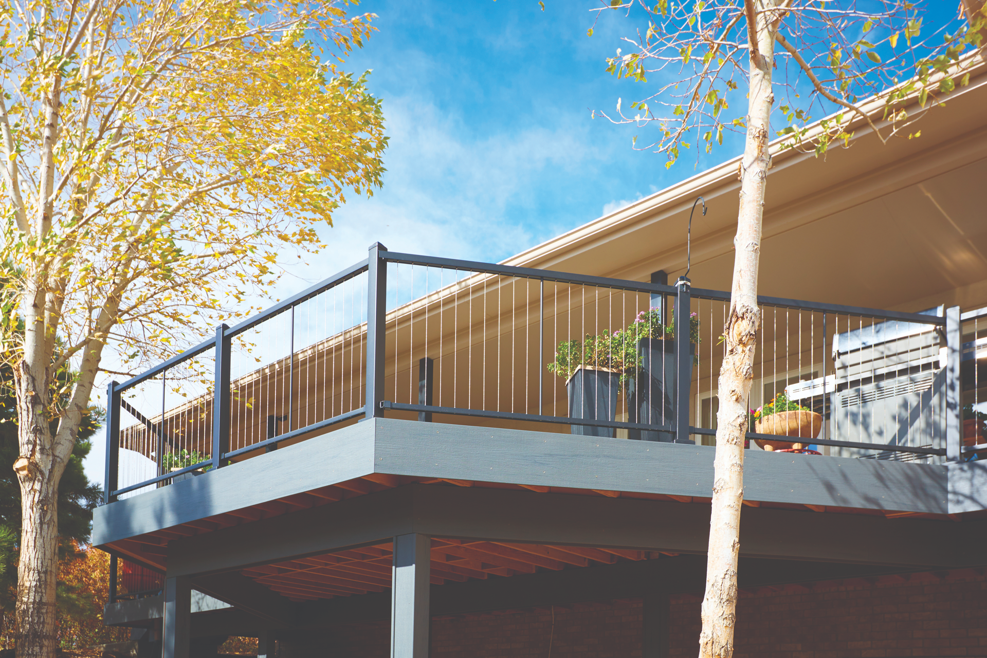 Second-story balcony with black metal cable railing against a blue-sky backdrop.