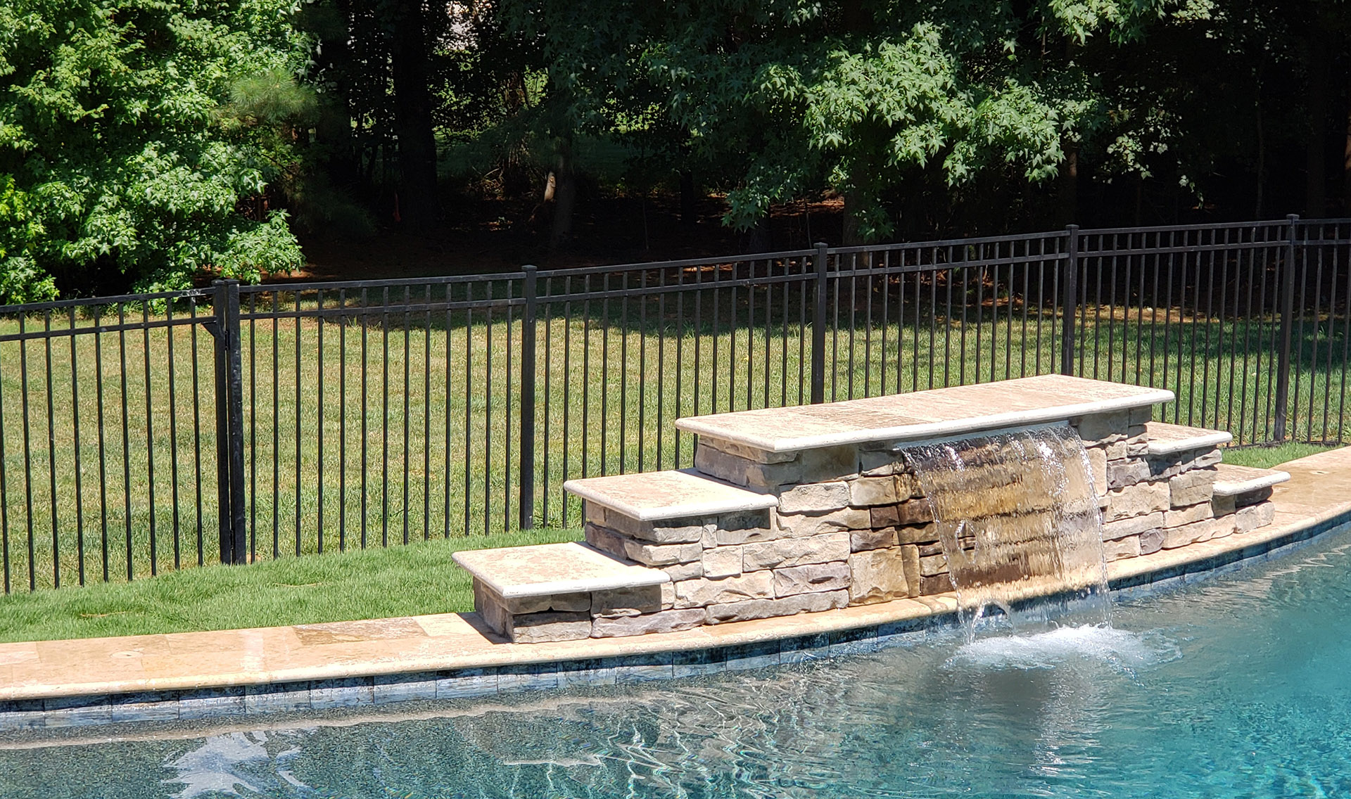 Backyard aluminum fencing beside a pool with waterfall and stone accents.