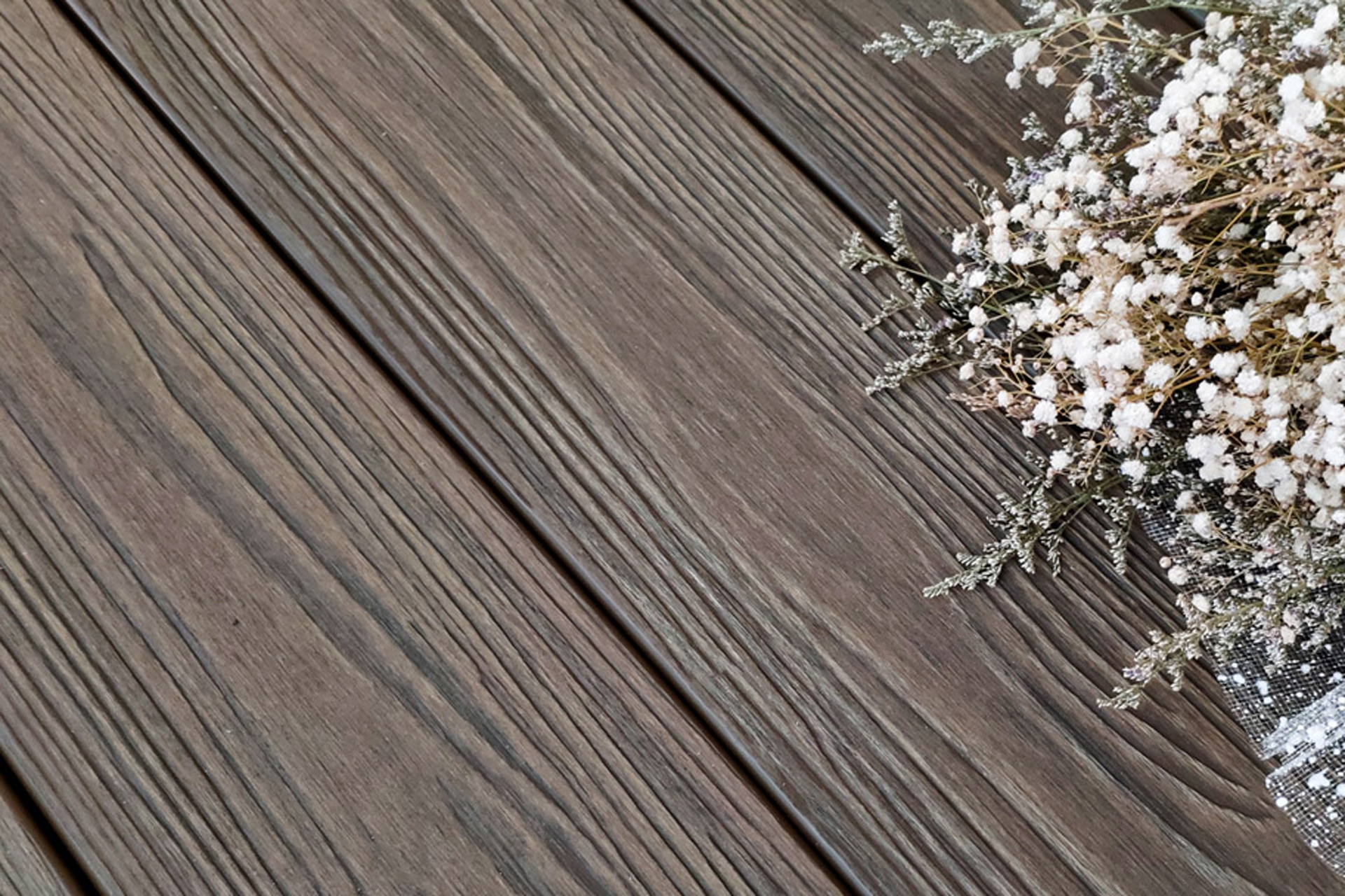 Close up view of dark composite deck boards showing the look-alike texture of wood with white flower bouquet off to the side. 