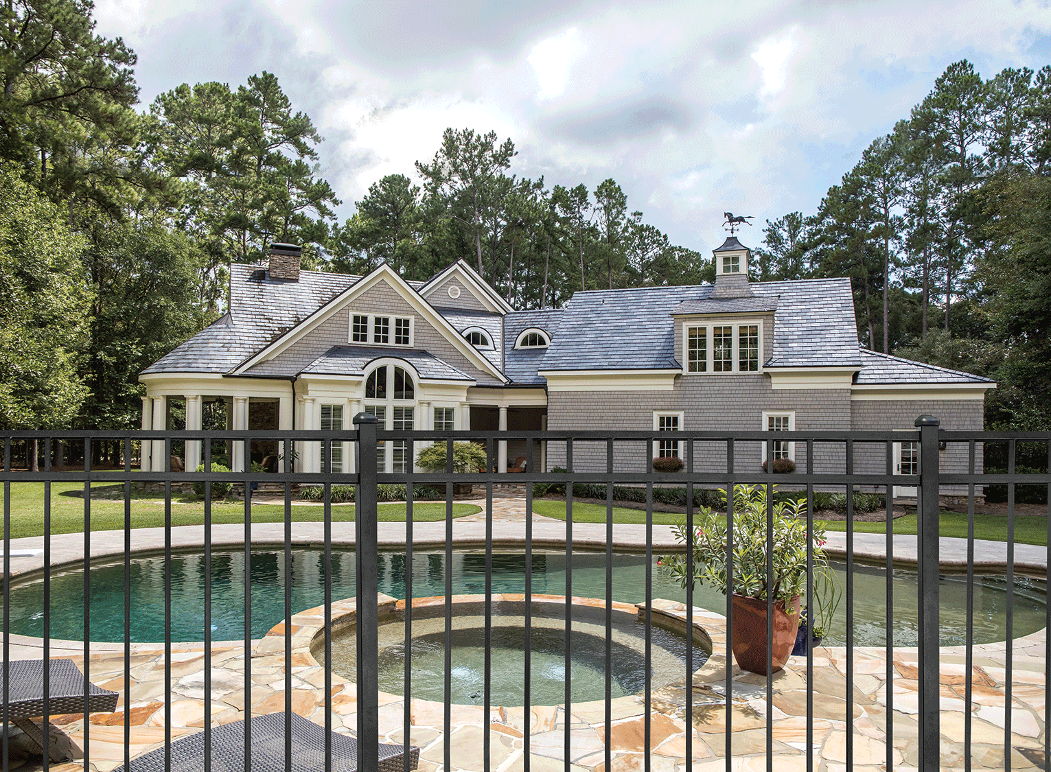 Black steel pool fence surrounding a modern home with hot tub and swimming pool.