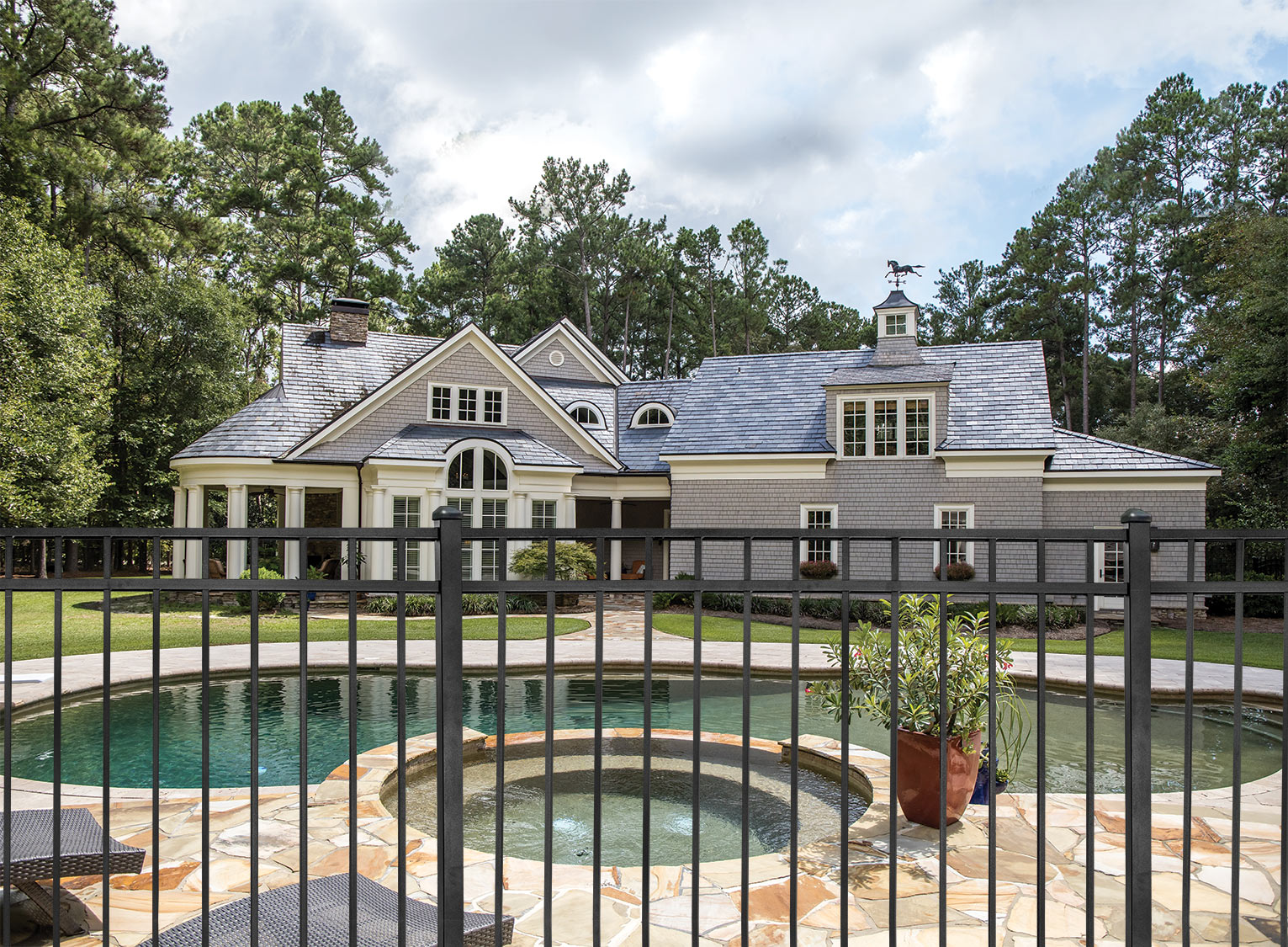 Aluminum fencing in the backyard of a property enclosing a pool and beautiful two-story house. 