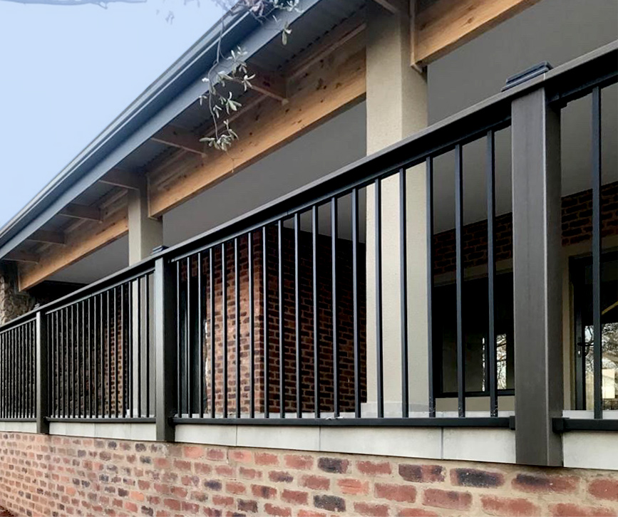 Powder-coated aluminum deck railing with vertical pickets installed along a covered patio.