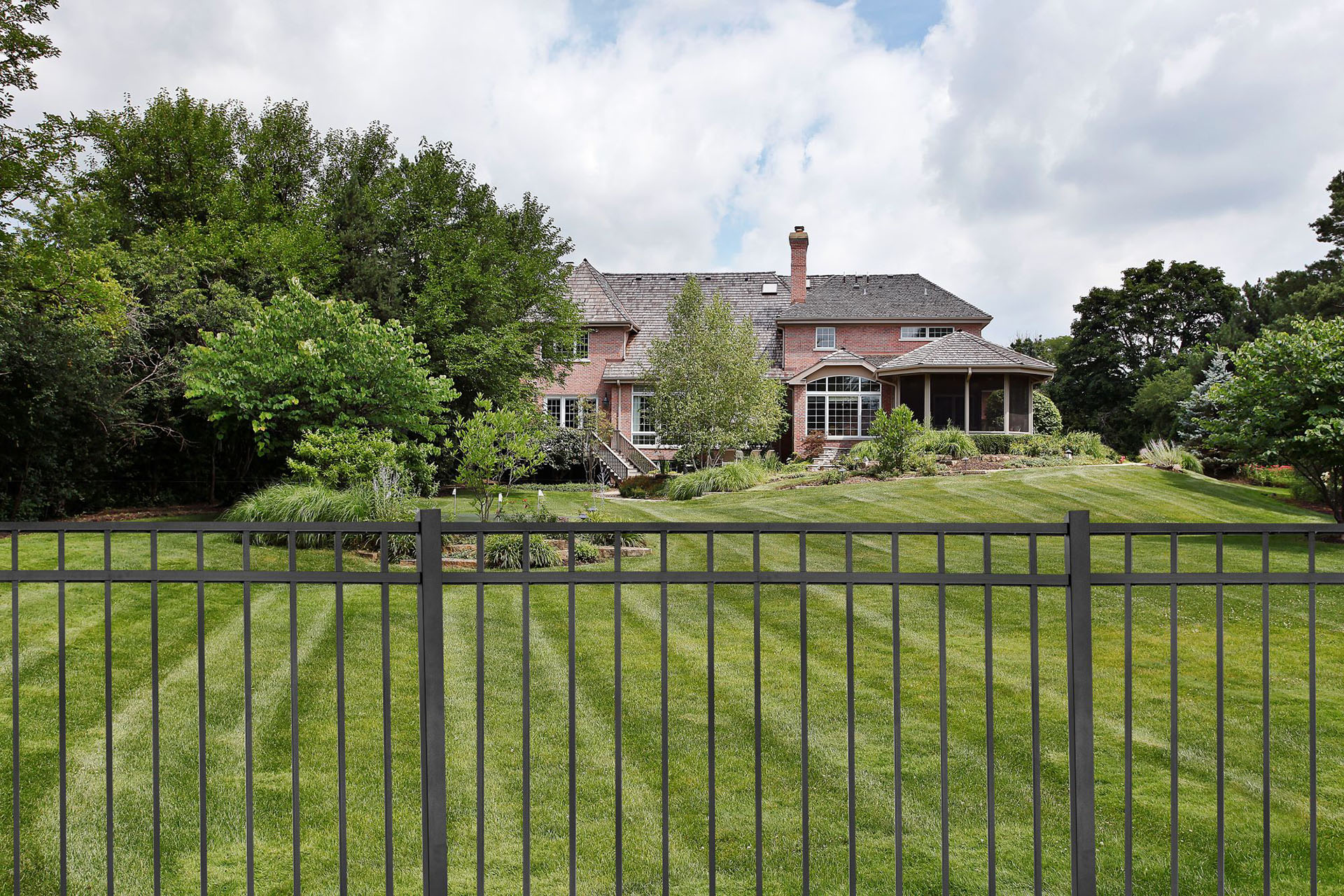 Aluminum fence enclosing a landscaped backyard behind a brick home.