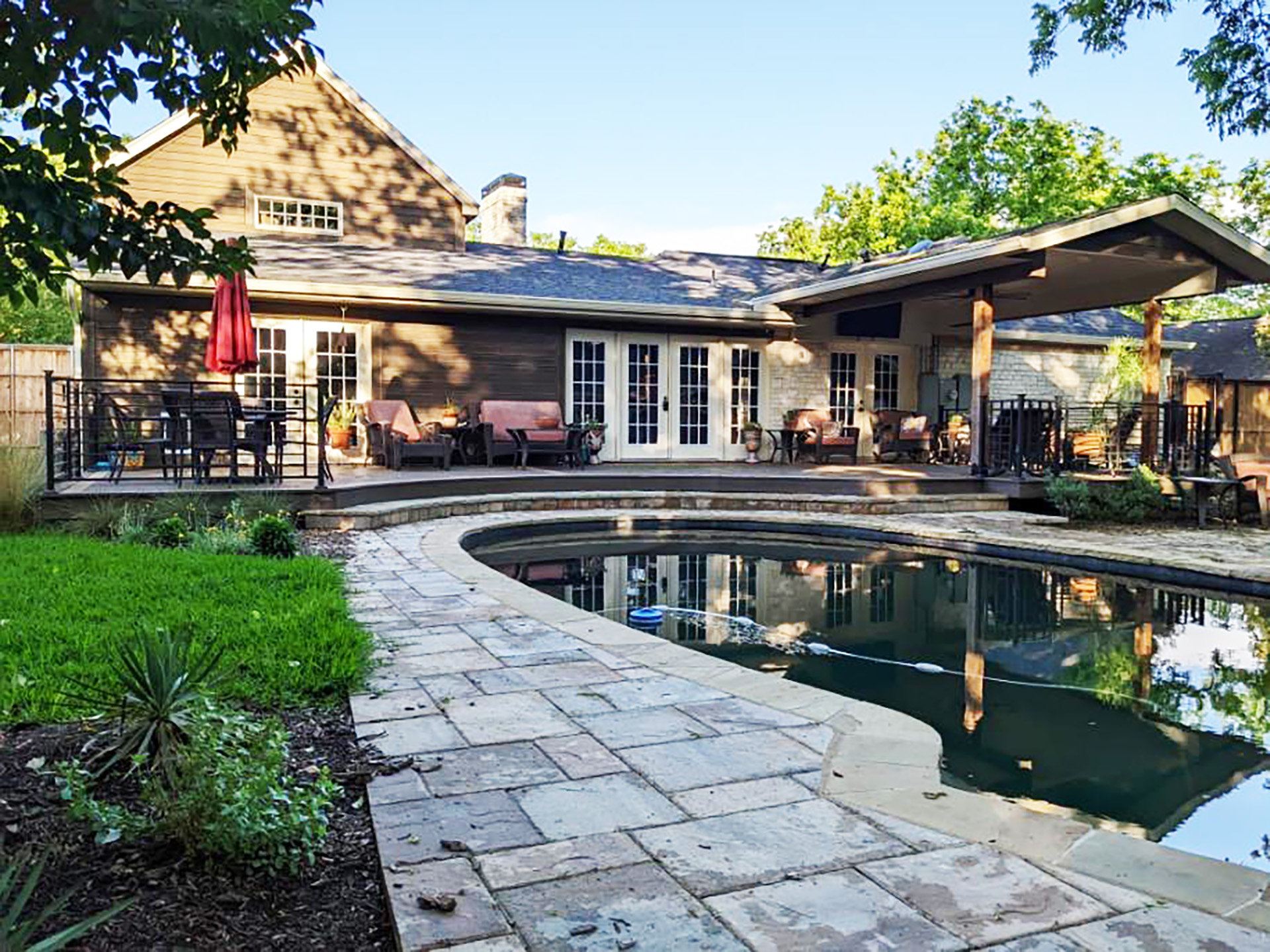 Backyard with a curved pool and a covered patio featuring modern steel deck railings