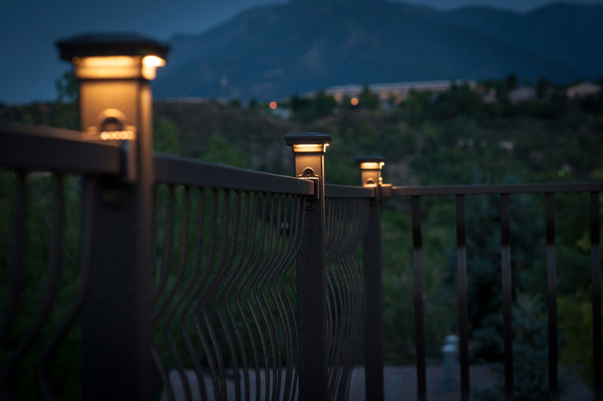 Close-up view of illuminated post cap lights on aluminum railings, showcasing lighting against a mountainous backdrop.