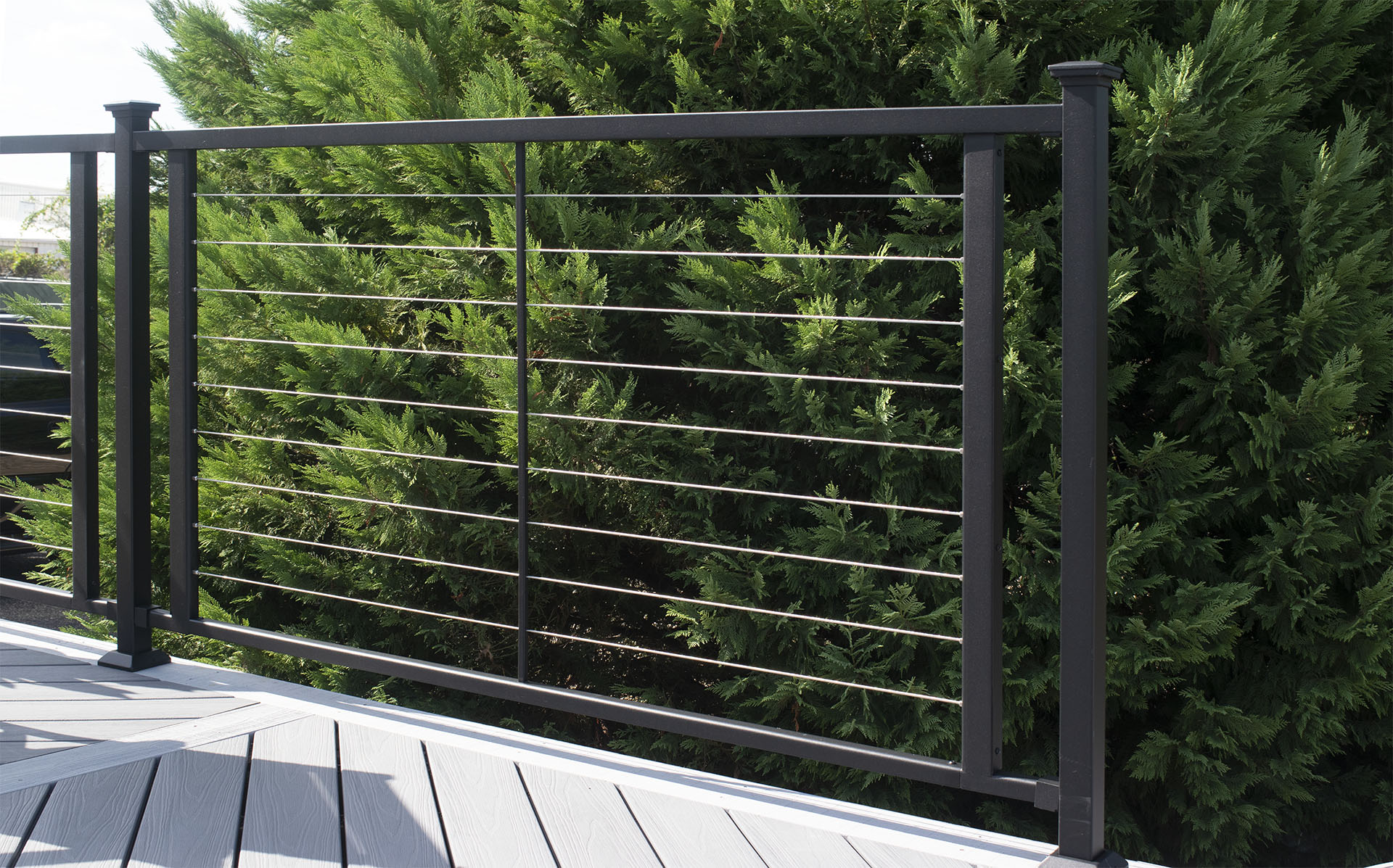 A black cable railing set against a backdrop of dense greenery, highlighting its functional design in outdoor spaces.