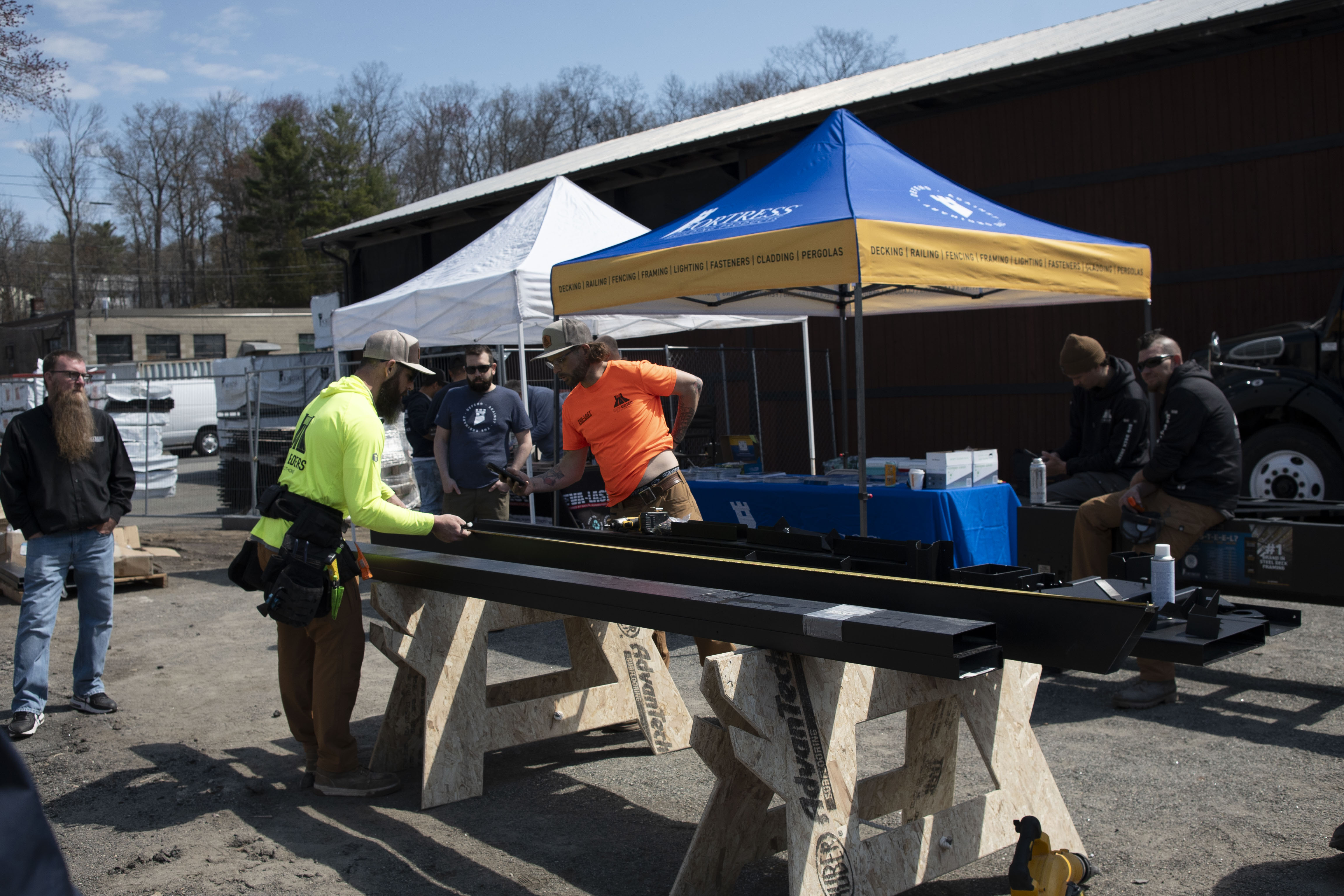 Tradesmen demonstrate steel deck framing installation under a Fortress Building Products tent at a professional builder workshop.