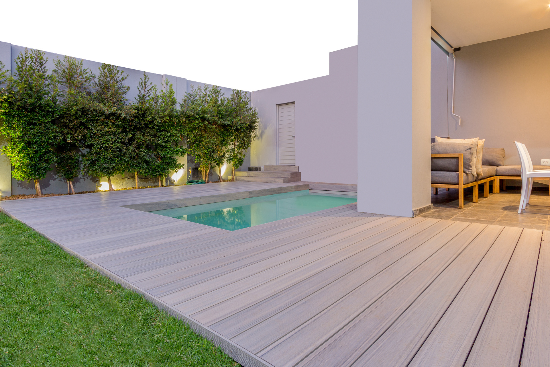 Composite decking next to a pool in a modern backyard with trees lining the exterior wall.