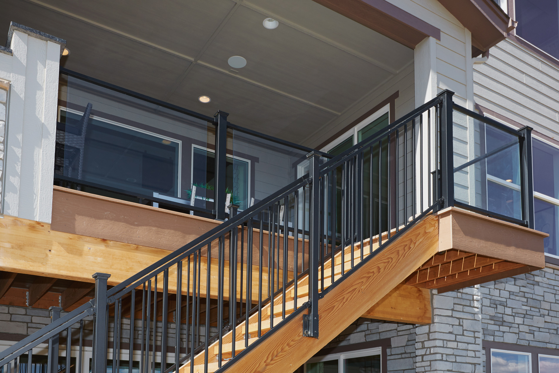 Deck stairs with steel railing in front of a balcony with glass railing