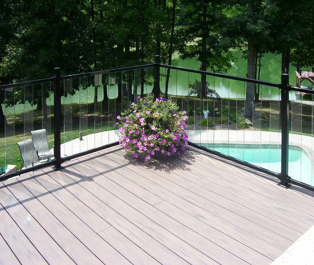 Metal deck railing with large purple flower planter on a deck with serene lake and pool in background.