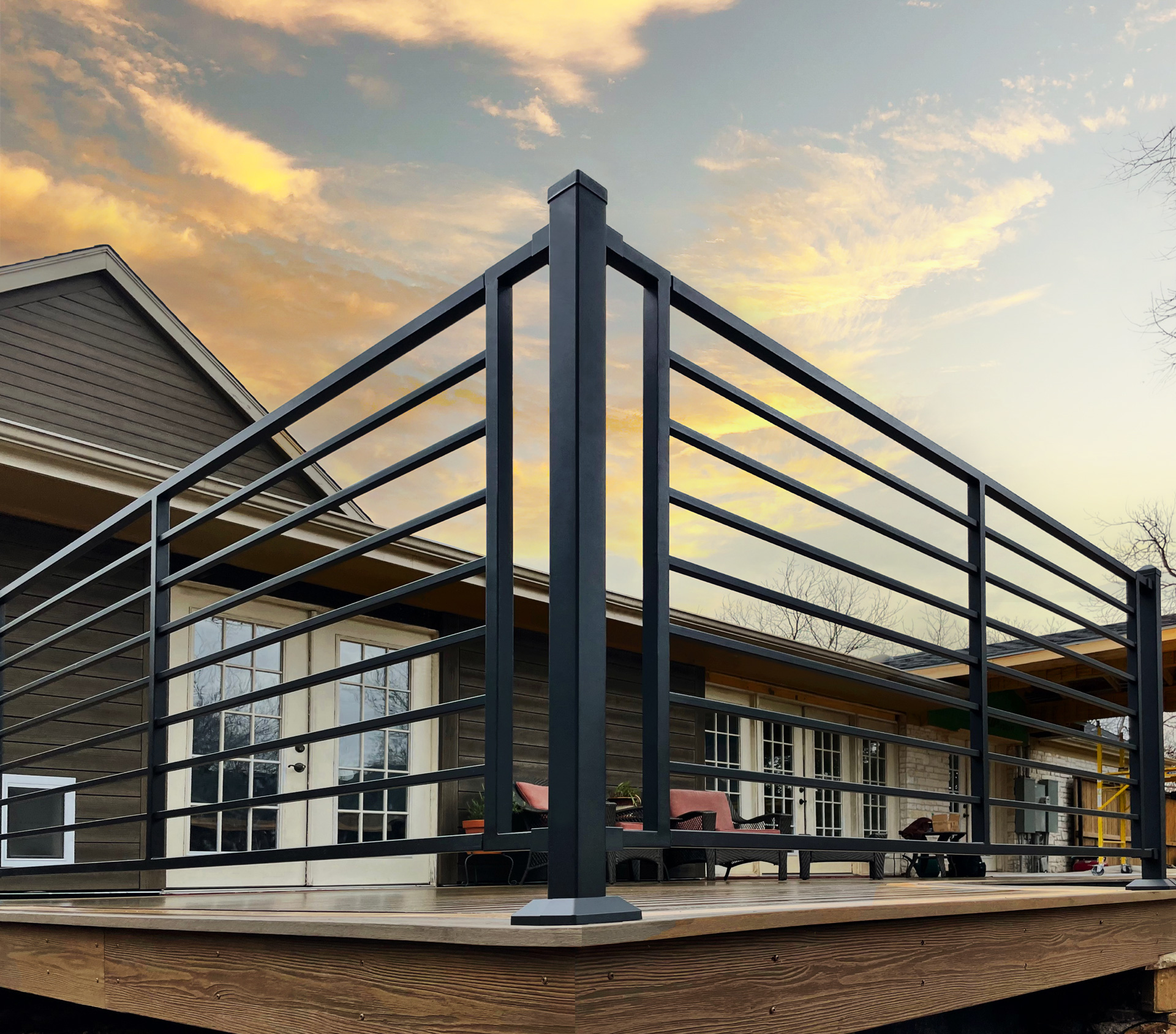 Black Metal deck railing shown enclosing a upper deck patio with the sun setting in the background. 