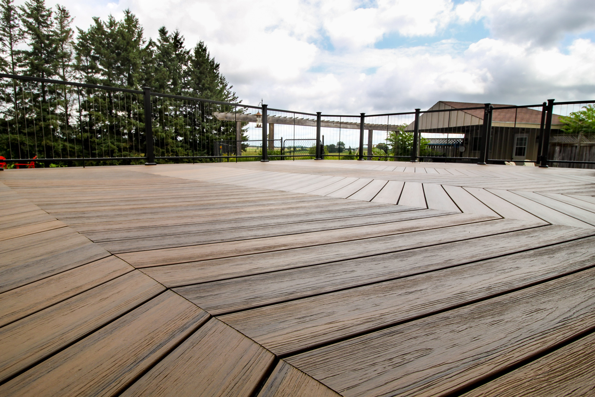 Close up view of composite decking with cable railing on the perimeter with tall trees in the background. 