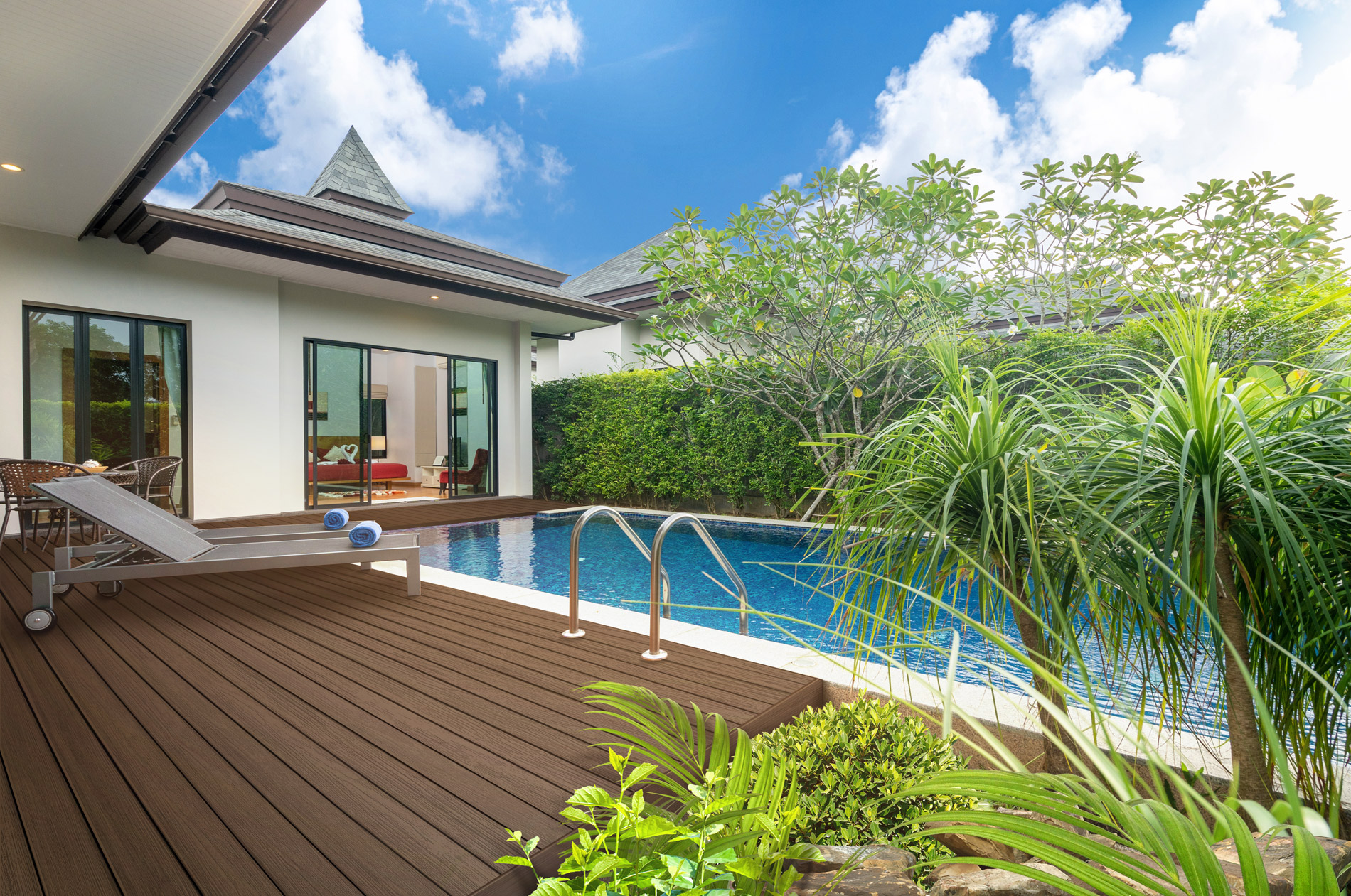 Composite decking shown poolside in a modern backyard with greenery as a perimeter.