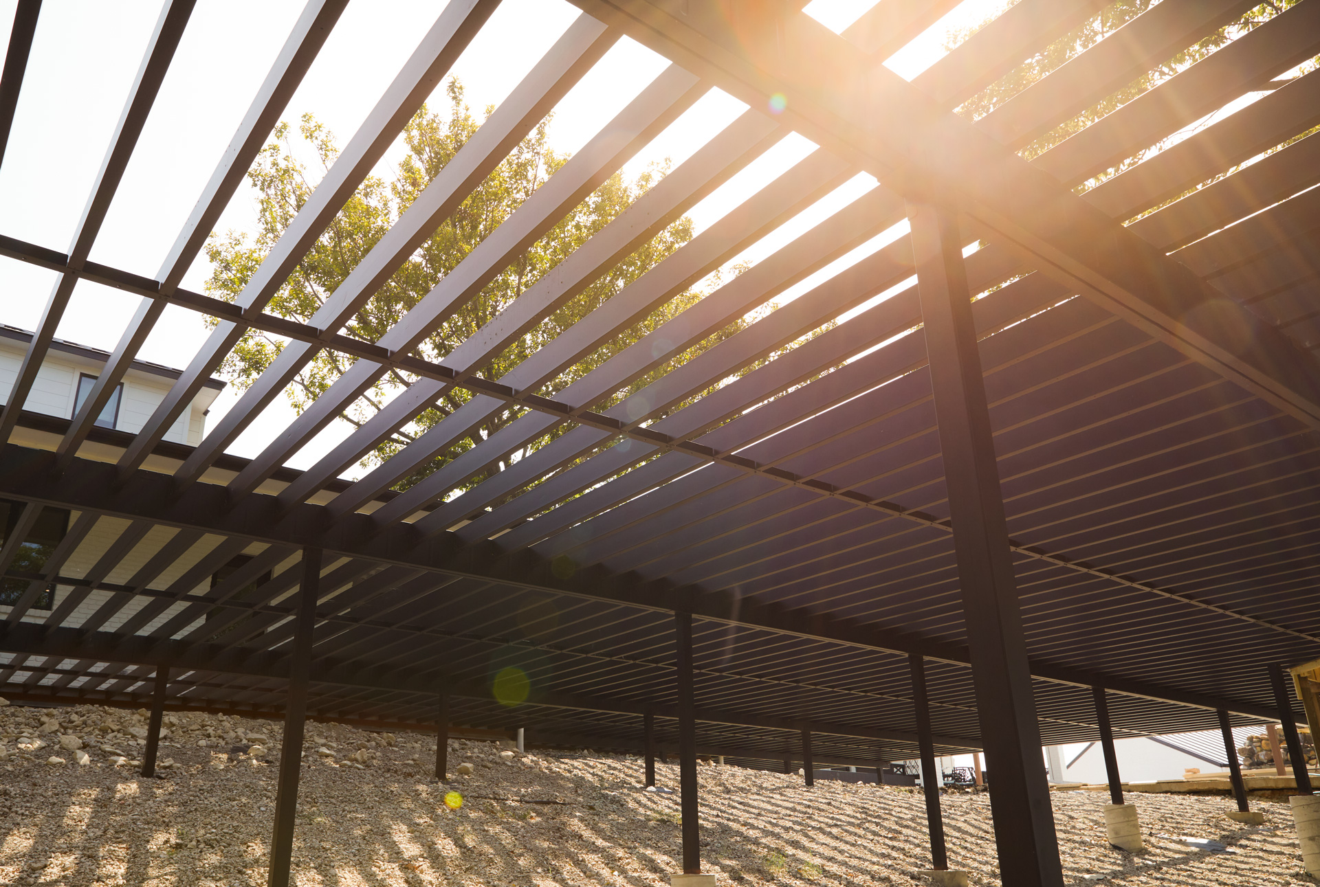 View from beneath a steel deck frame with a tree and sunlight shining through the beams. 