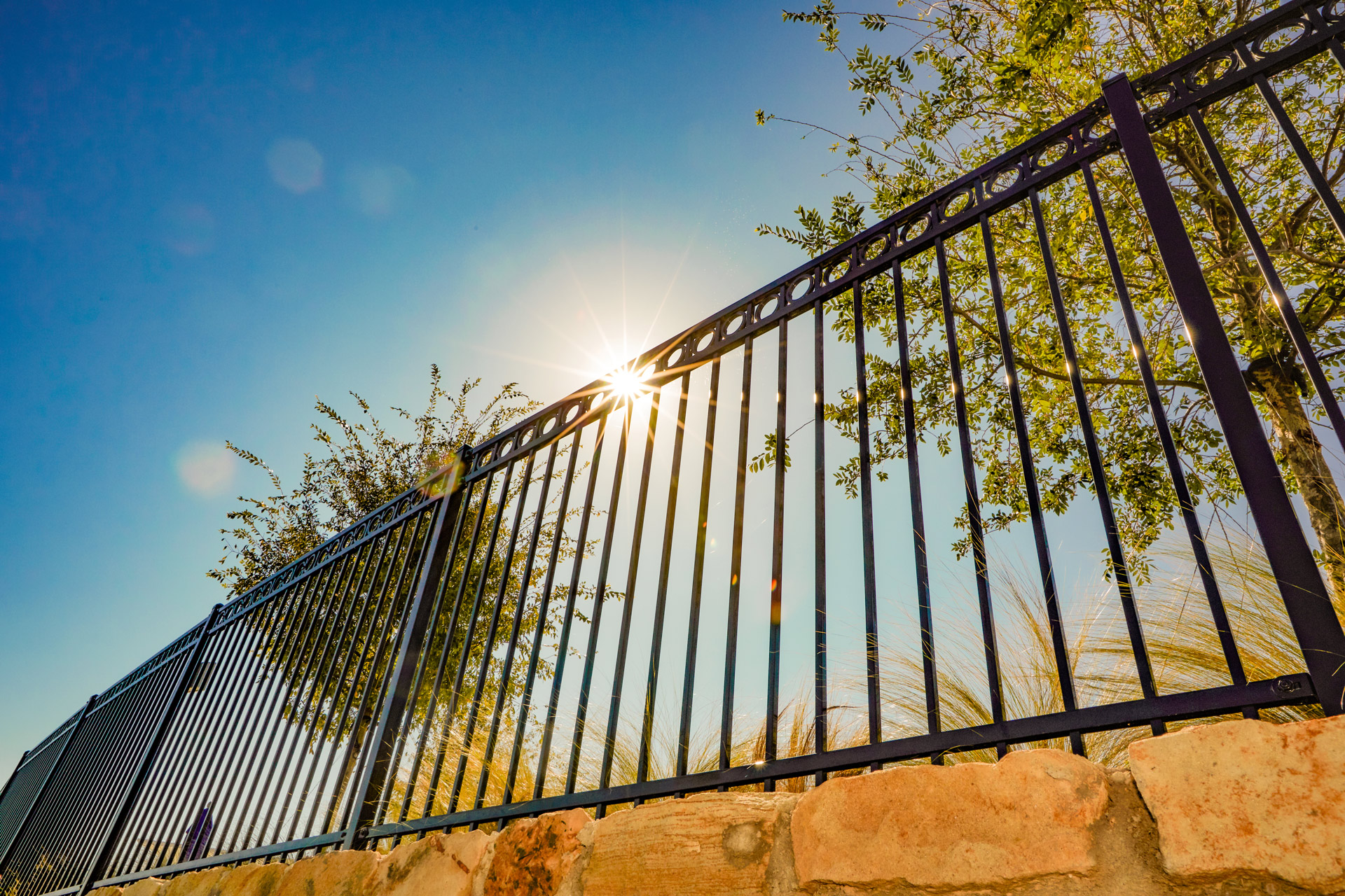 View from below a steel fence panel with sun glaring in the background.