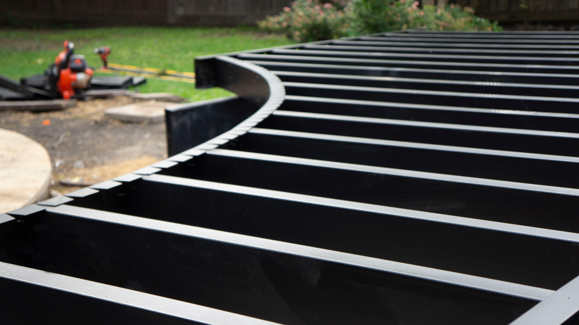 Black curved deck framing with tools in the background.