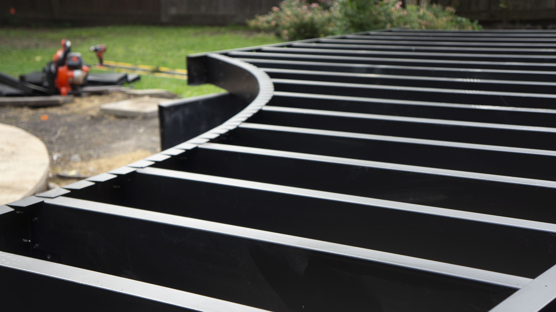 Curved steel deck framing with evenly spaced joists in a backyard setting.
