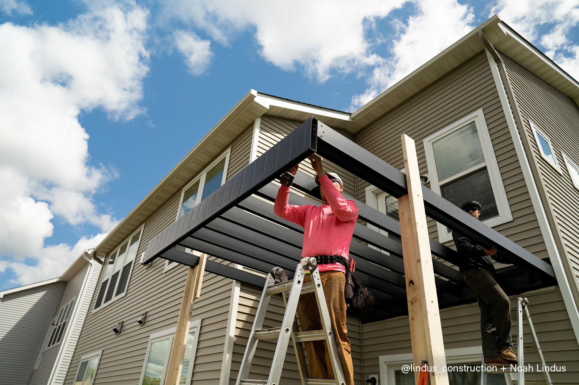 Two men engaged in building a pergola on a house's multi-level deck area
