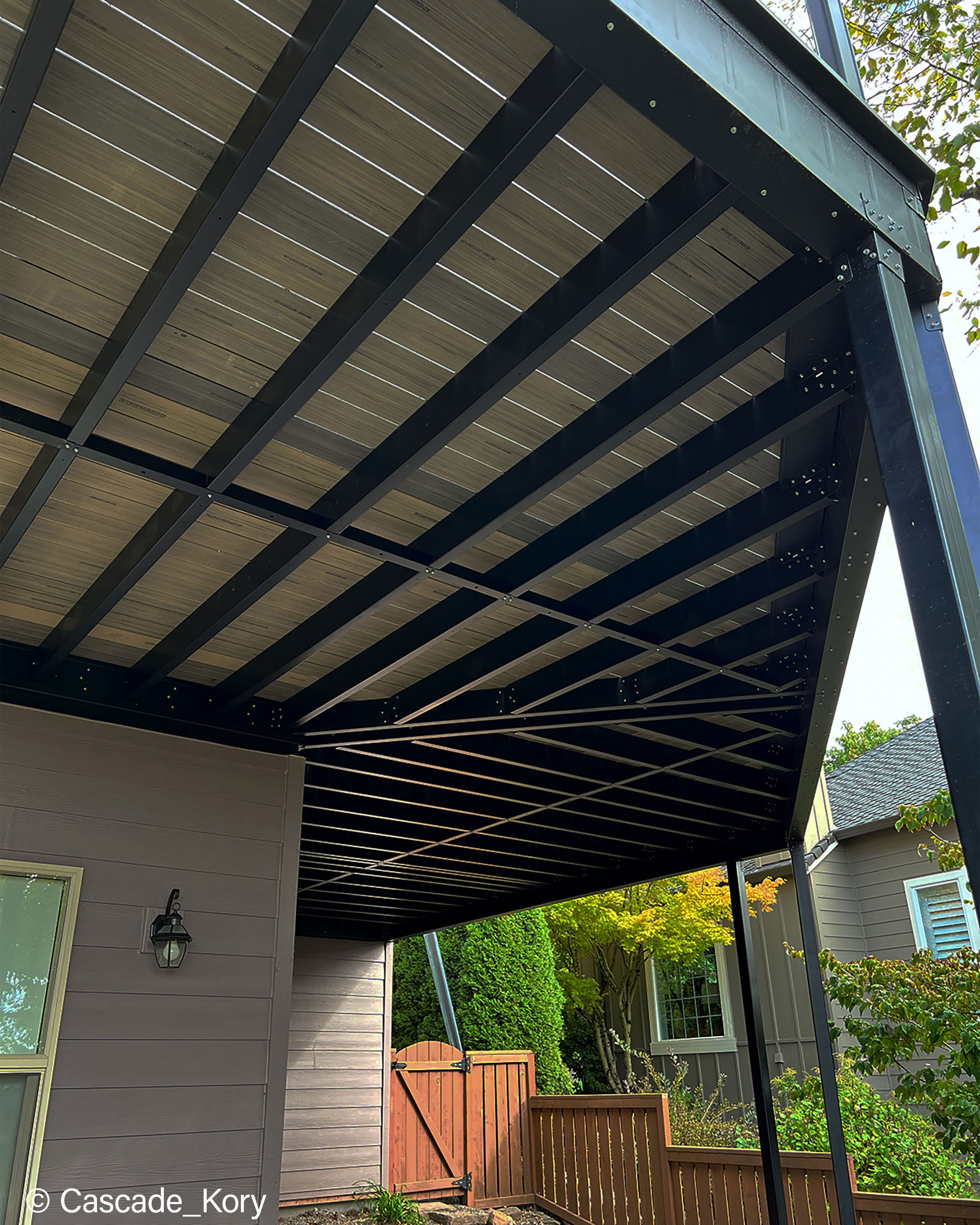 Underneath view of steel deck frame for upper deck with shrubs in background.