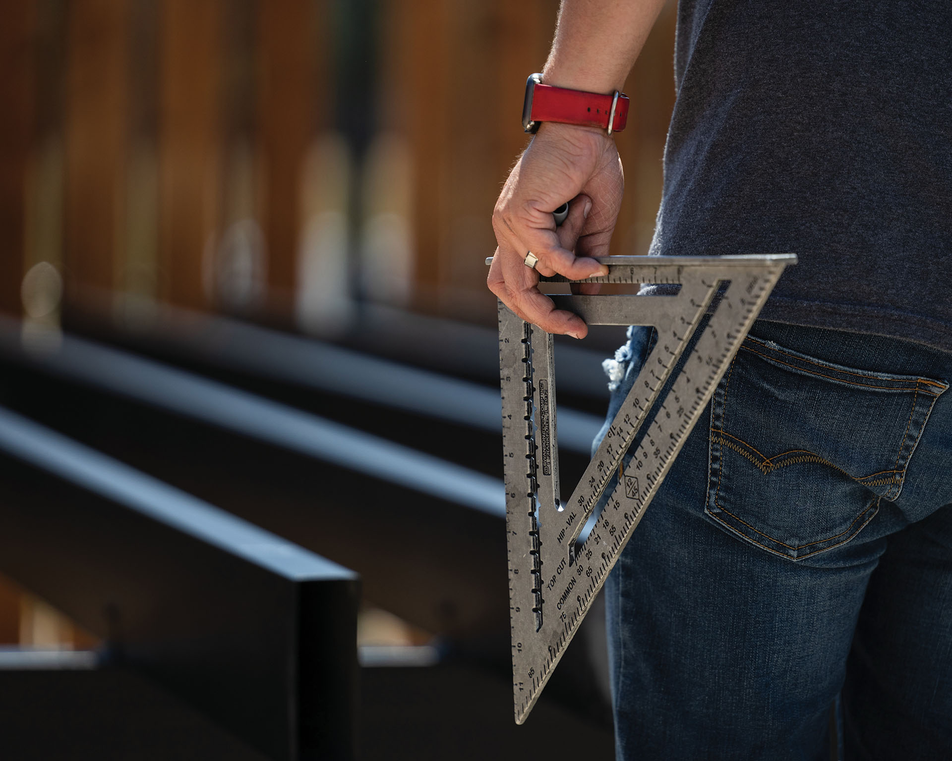 Close-up of a builder holding a square ruler while inspecting steel joists during deck framing.