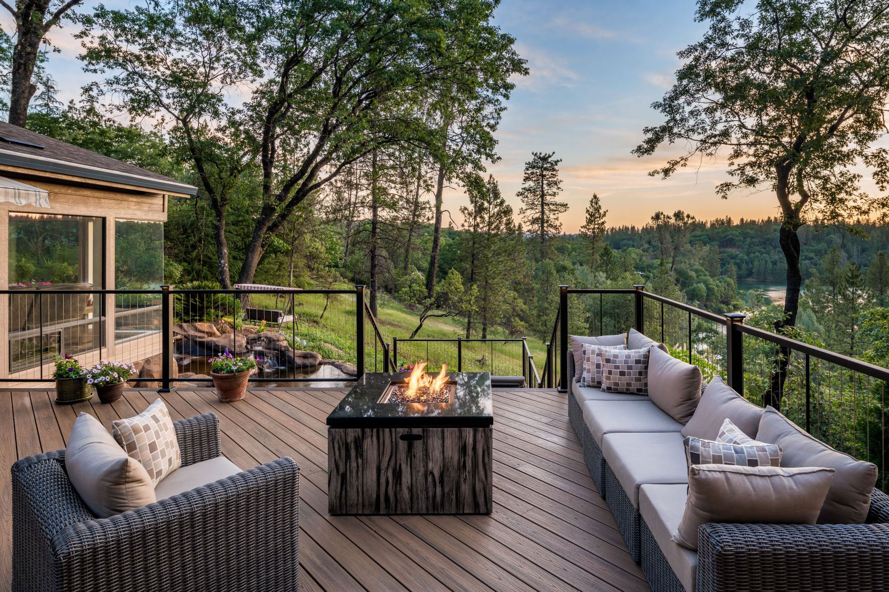 Outdoor living area with couches around a fireplace and the sun setting over the trees in the background.