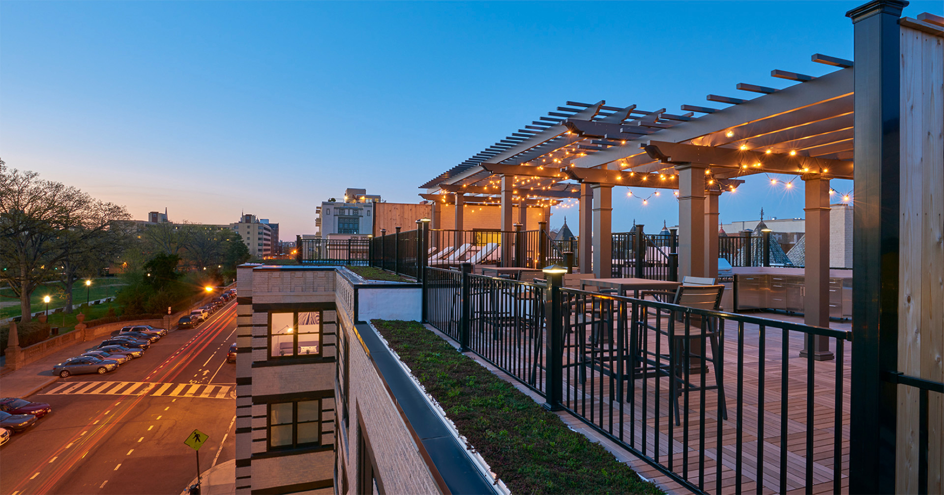 Modern roof deck at sunset with steel railing and pergolas with hanging lights creating an outdoor living space.