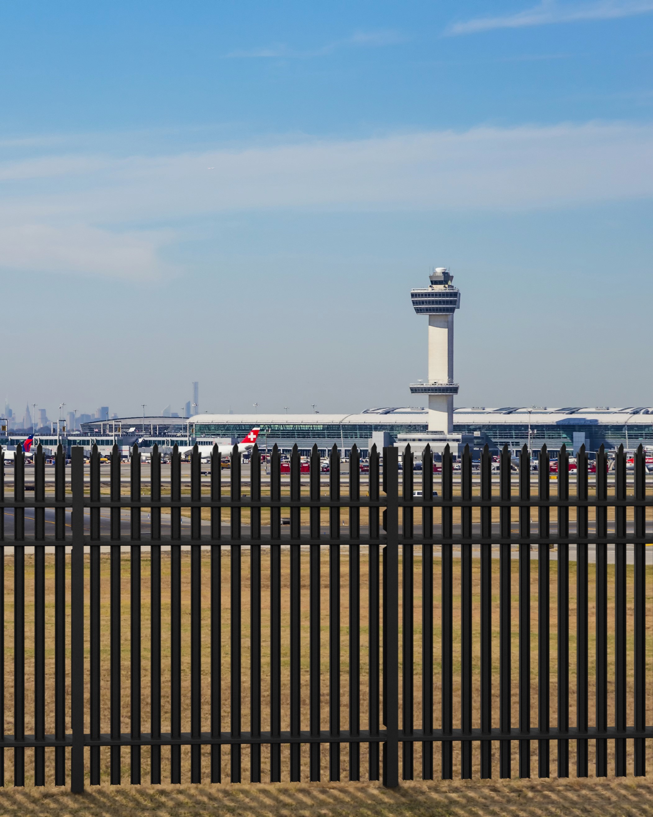 Steel high-security perimeter fence protecting airport property with control tower in background.
