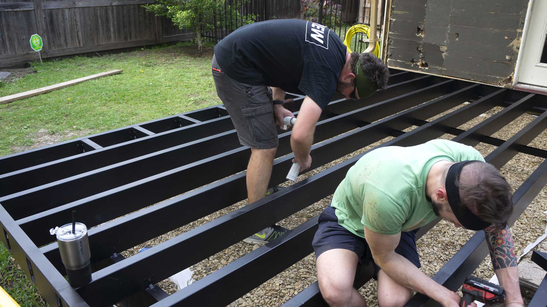 Two workers assembling a steel deck substructure in a backyard.