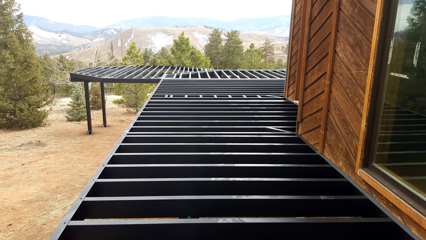 Steel deck framing attached to a rustic house overlooking the mountains.