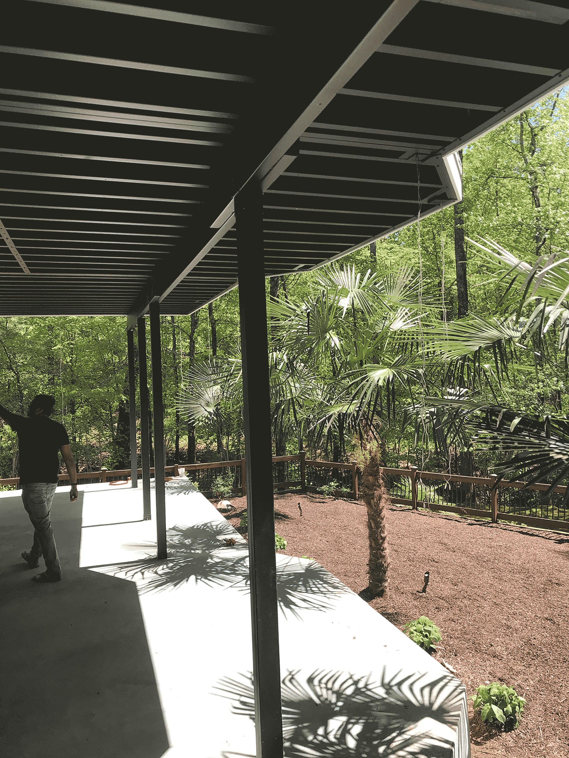 Underneath black steel deck framing with man walking towards tropical greenery.