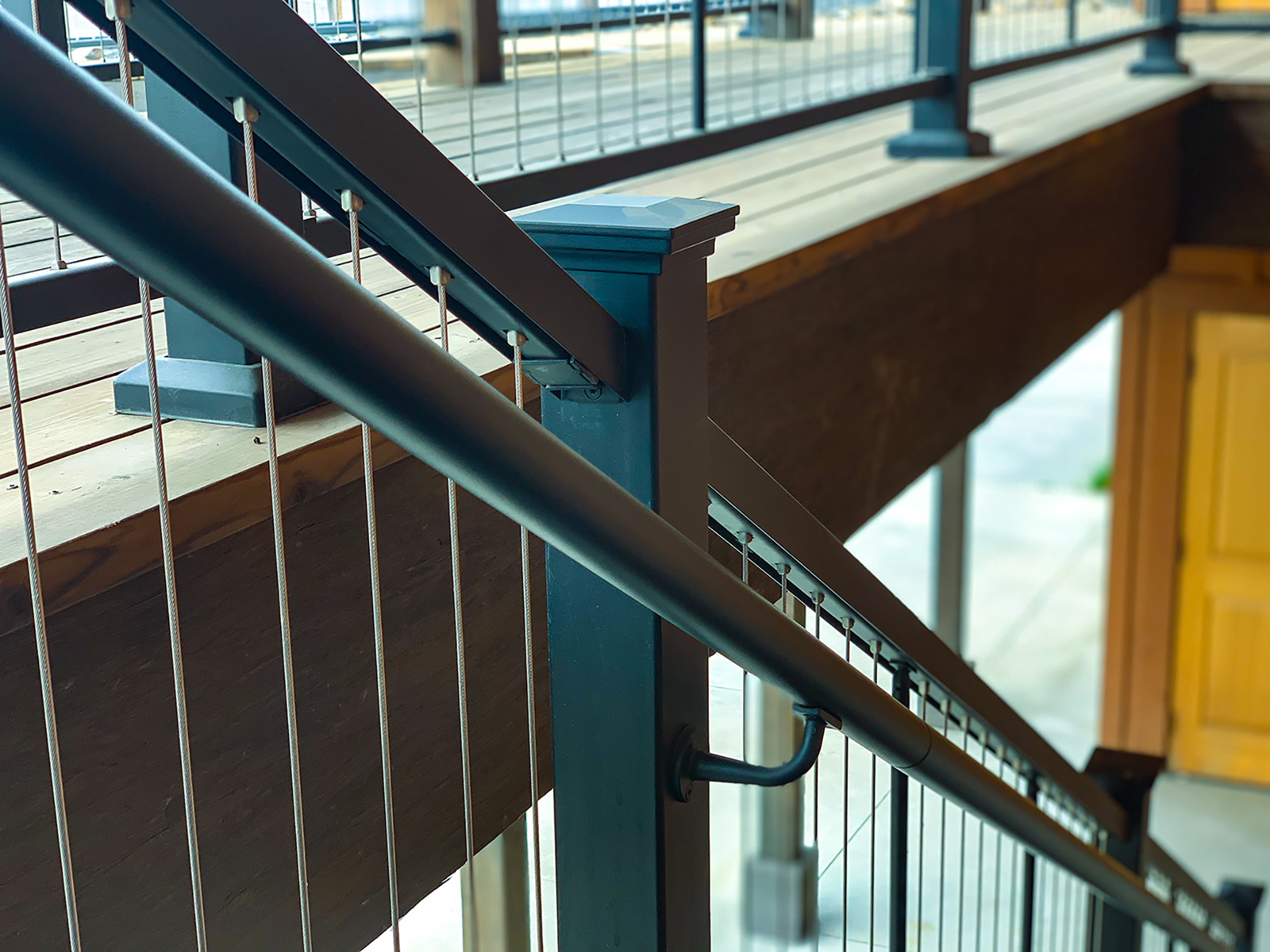 Close up view of cable railings on stairs, showing a yellow door at the bottom of the stairs.