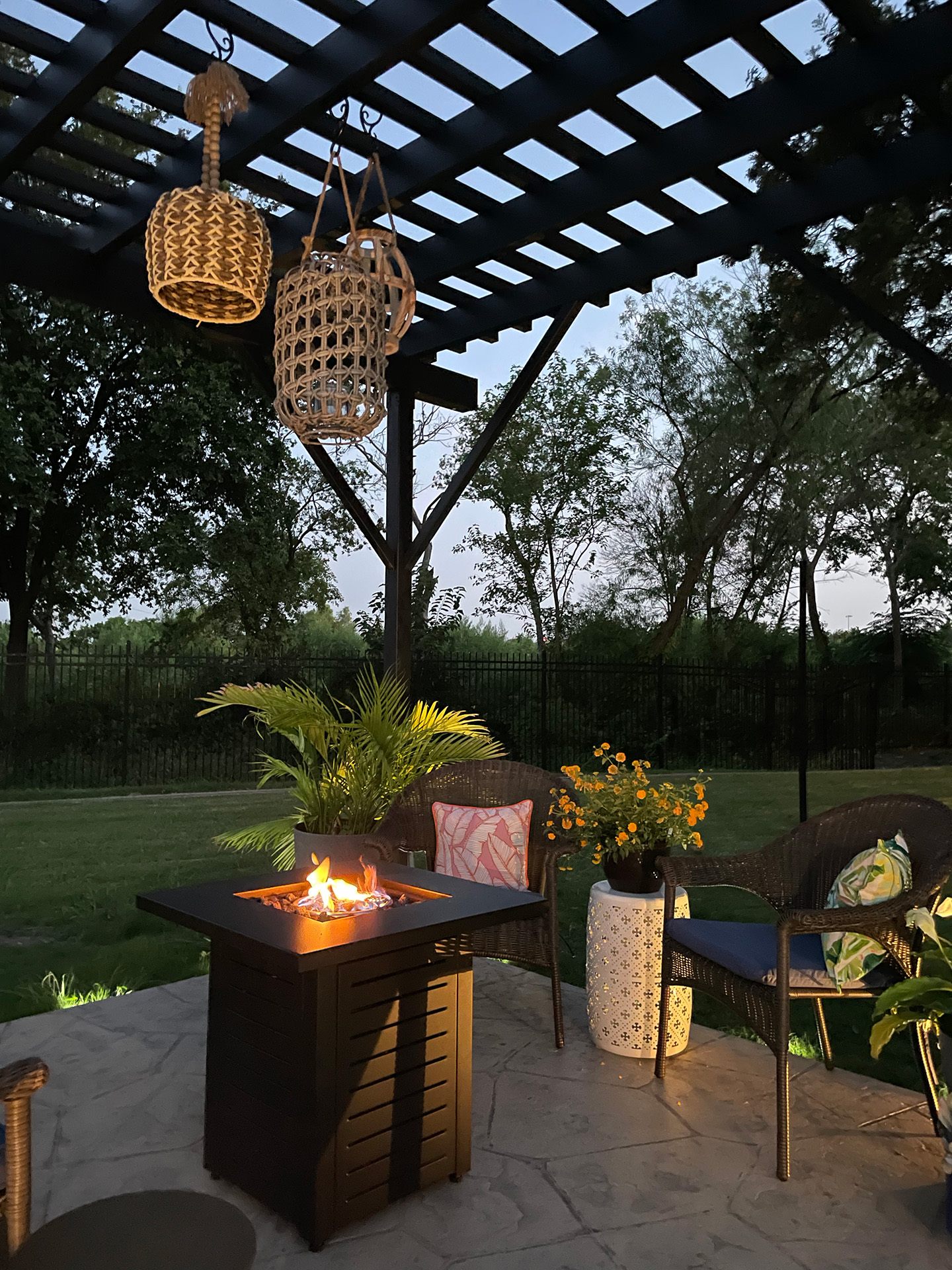 Chairs surrounding a small firepit underneath a standalone pergola. 