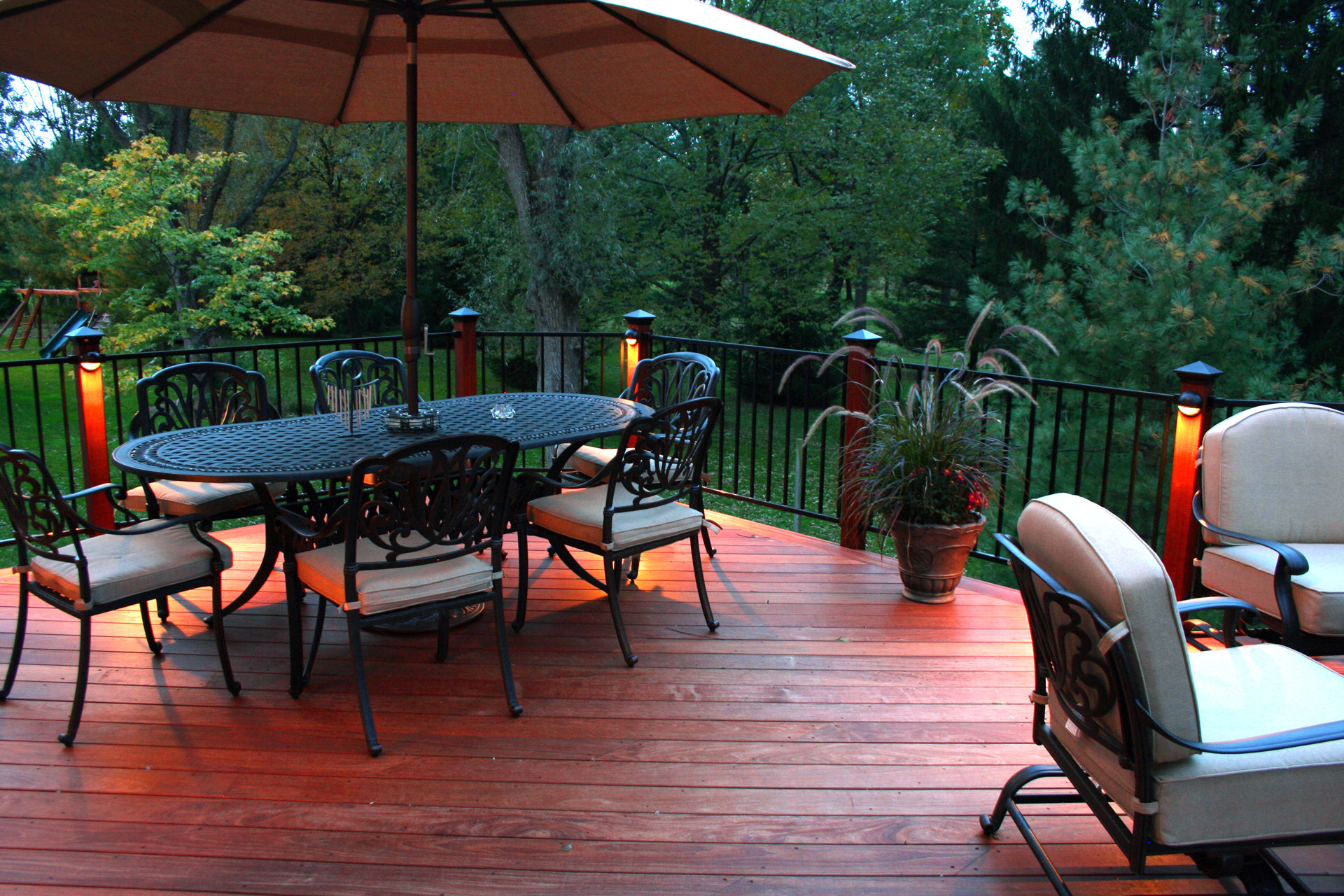 Outdoor dining area on a wooden deck, featuring light on aluminum railings.