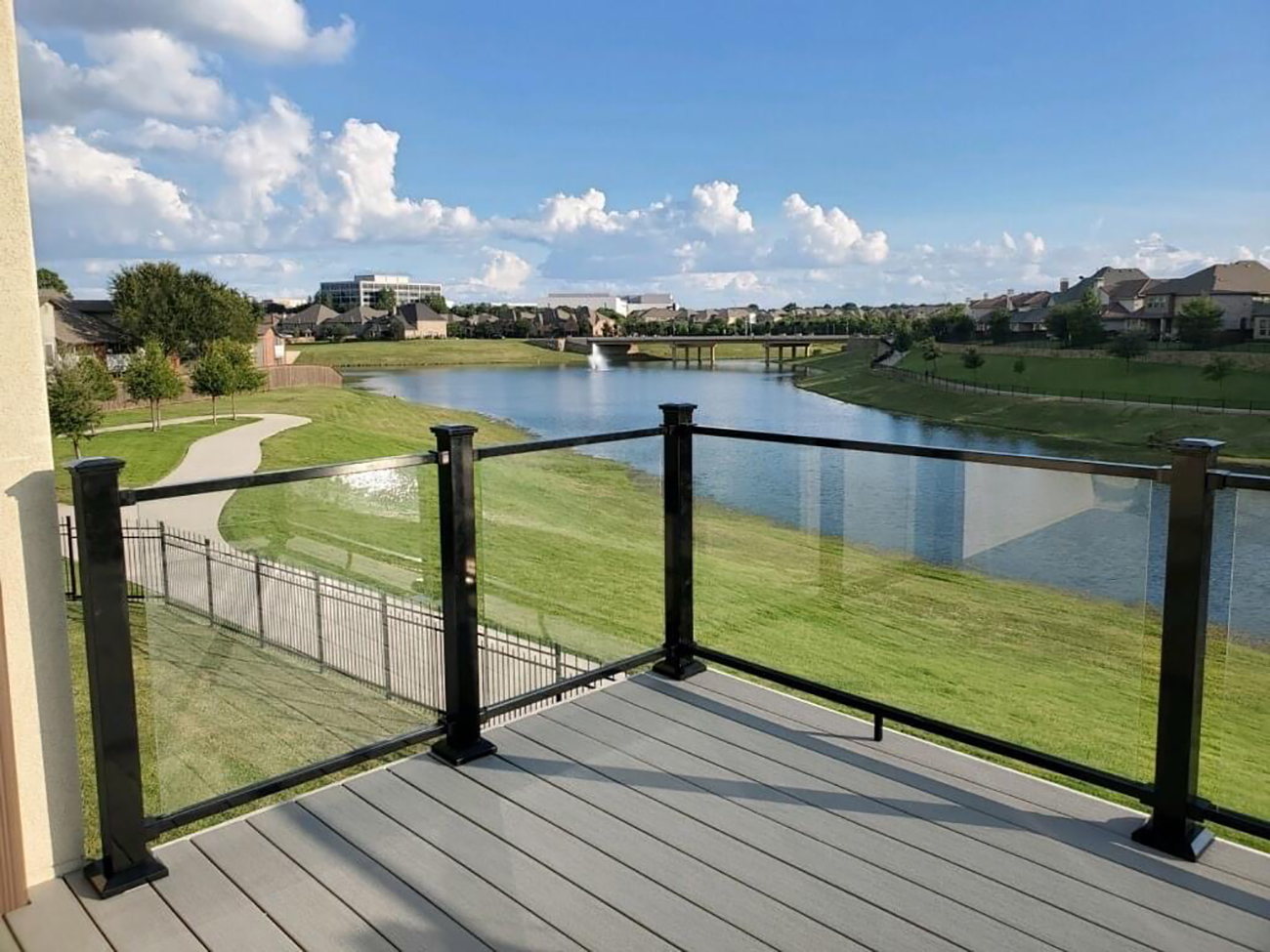 Deck with black metal and glass railing overlooking a pond and green landscape.