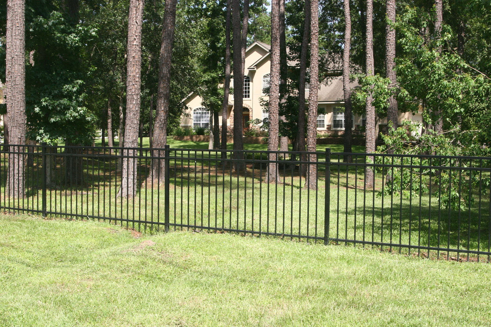 A durable, fire-resistant steel fence encloses a wooded backyard, providing a WUI-compliant perimeter to safeguard homes from wildfire risks.