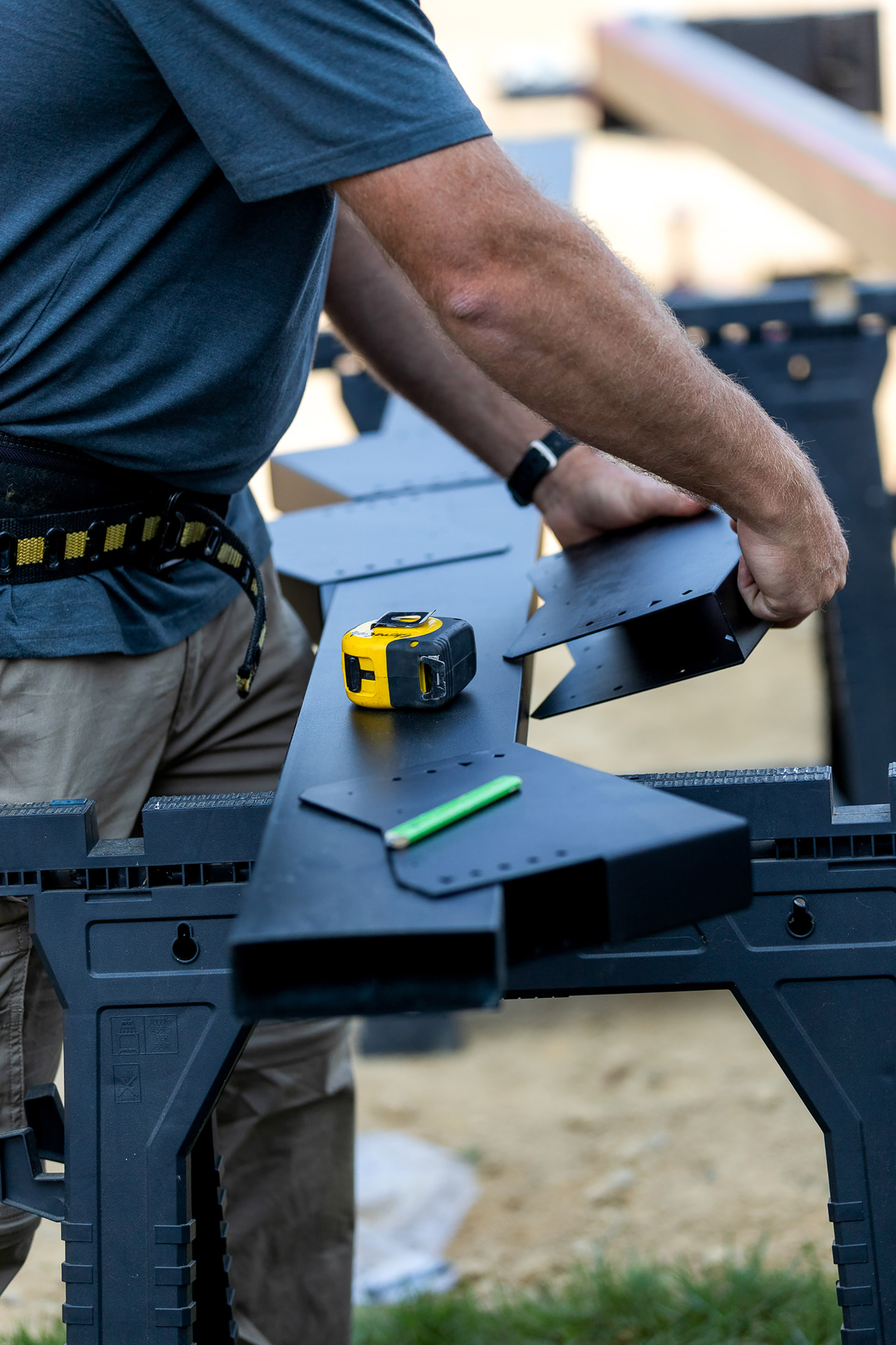 Contractor assembling steel deck components on sawhorses with measuring tools and fasteners.