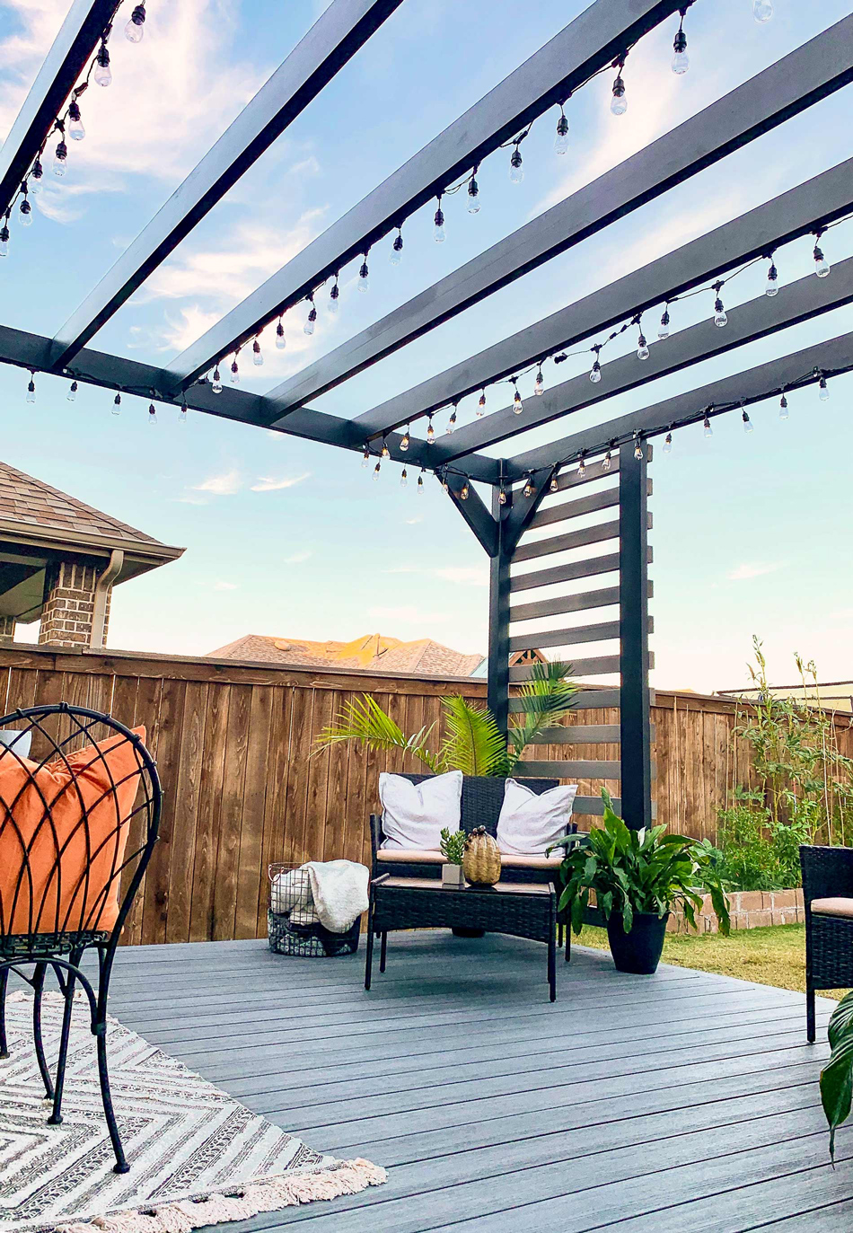 Backyard steel pergola with lights overhead and a seating are for an outdoor living space.