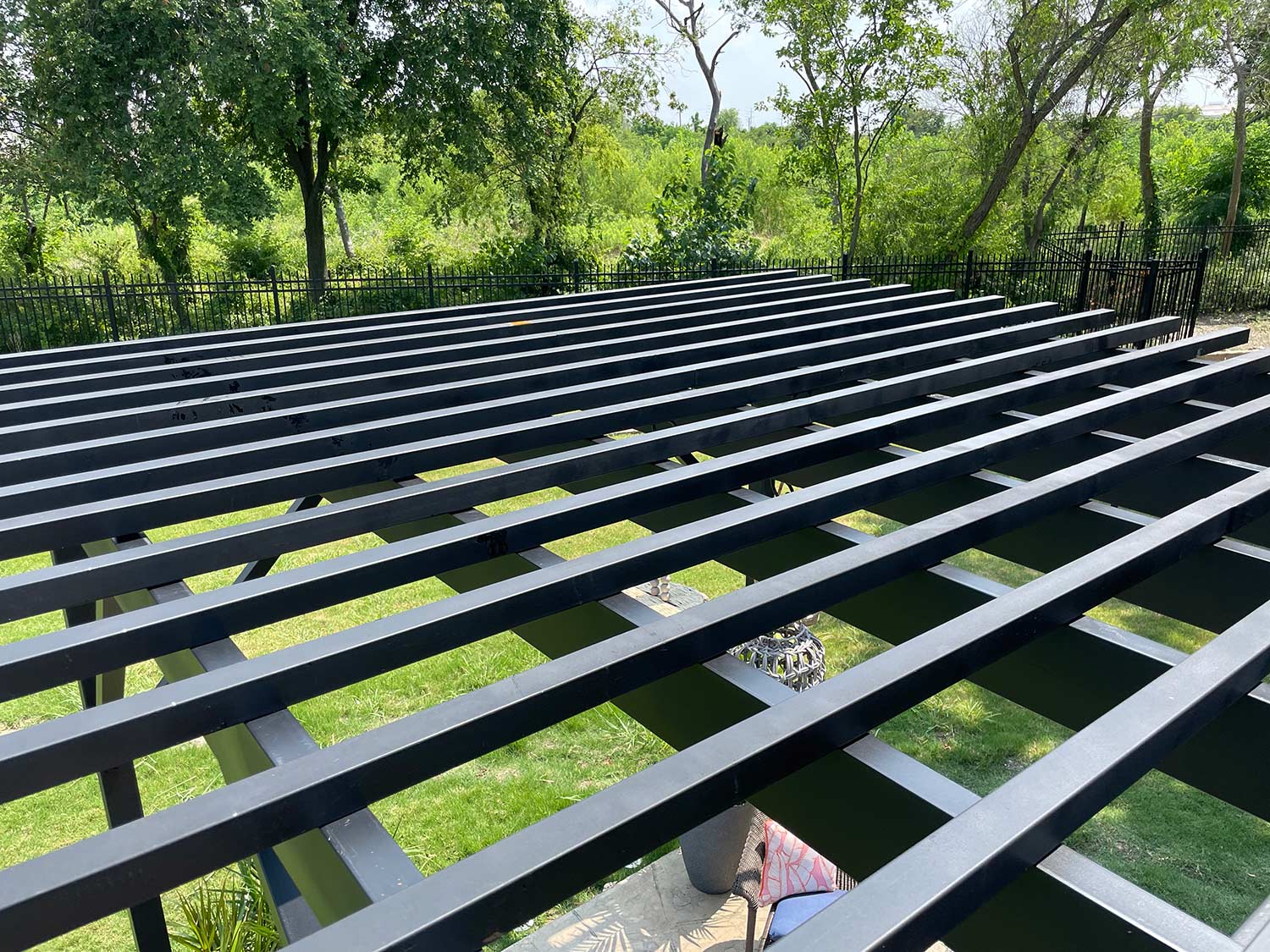 Above view of steel pergola with greenery in the background.