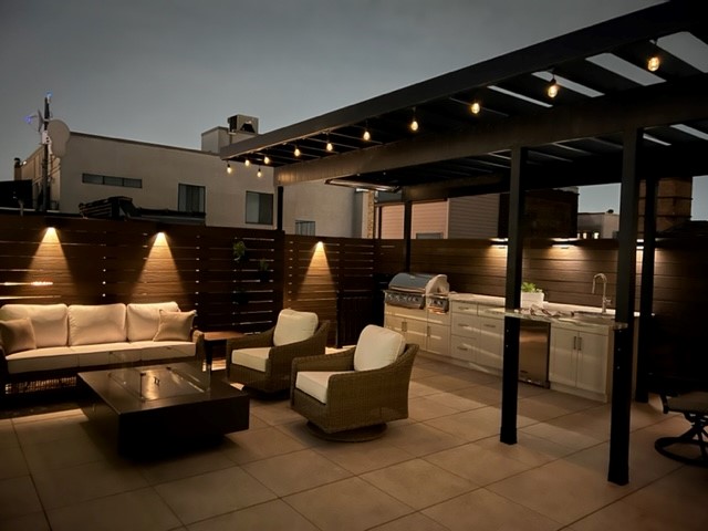 Outdoor patio space on a rooftop deck with a steel pergola over an outdoor kitchen space.