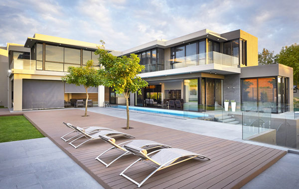 Panoramic view of a modern house with lawn chairs poolside on a composite deck.
