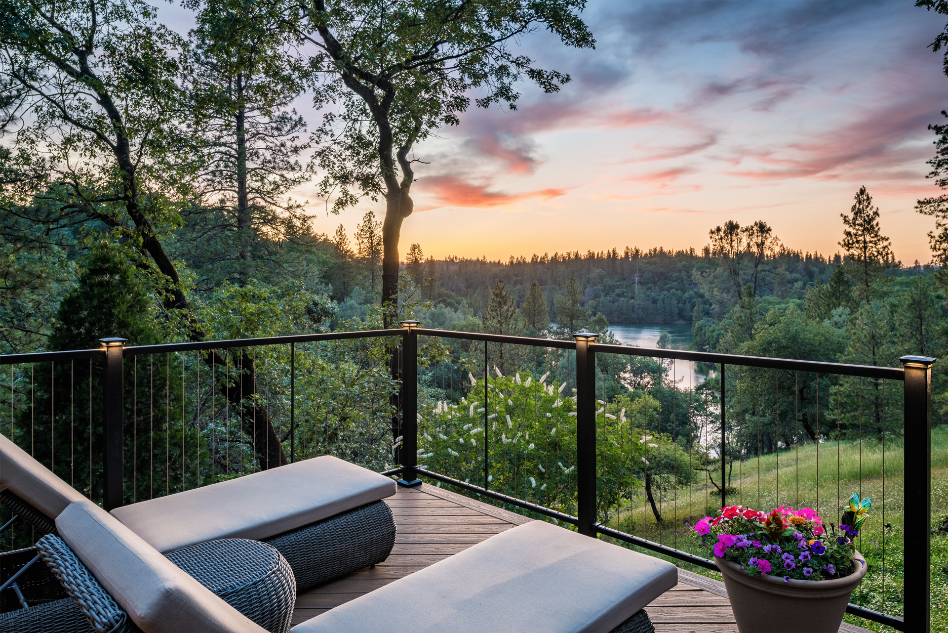 Deck with metal cable railing overlooking a lake and wooded area at sunset.