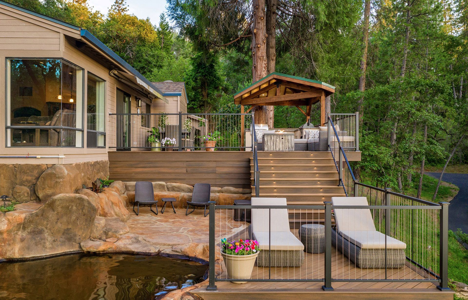 An outdoor deck featuring cable railing, with lounge chairs, a small table, and a covered seating area.